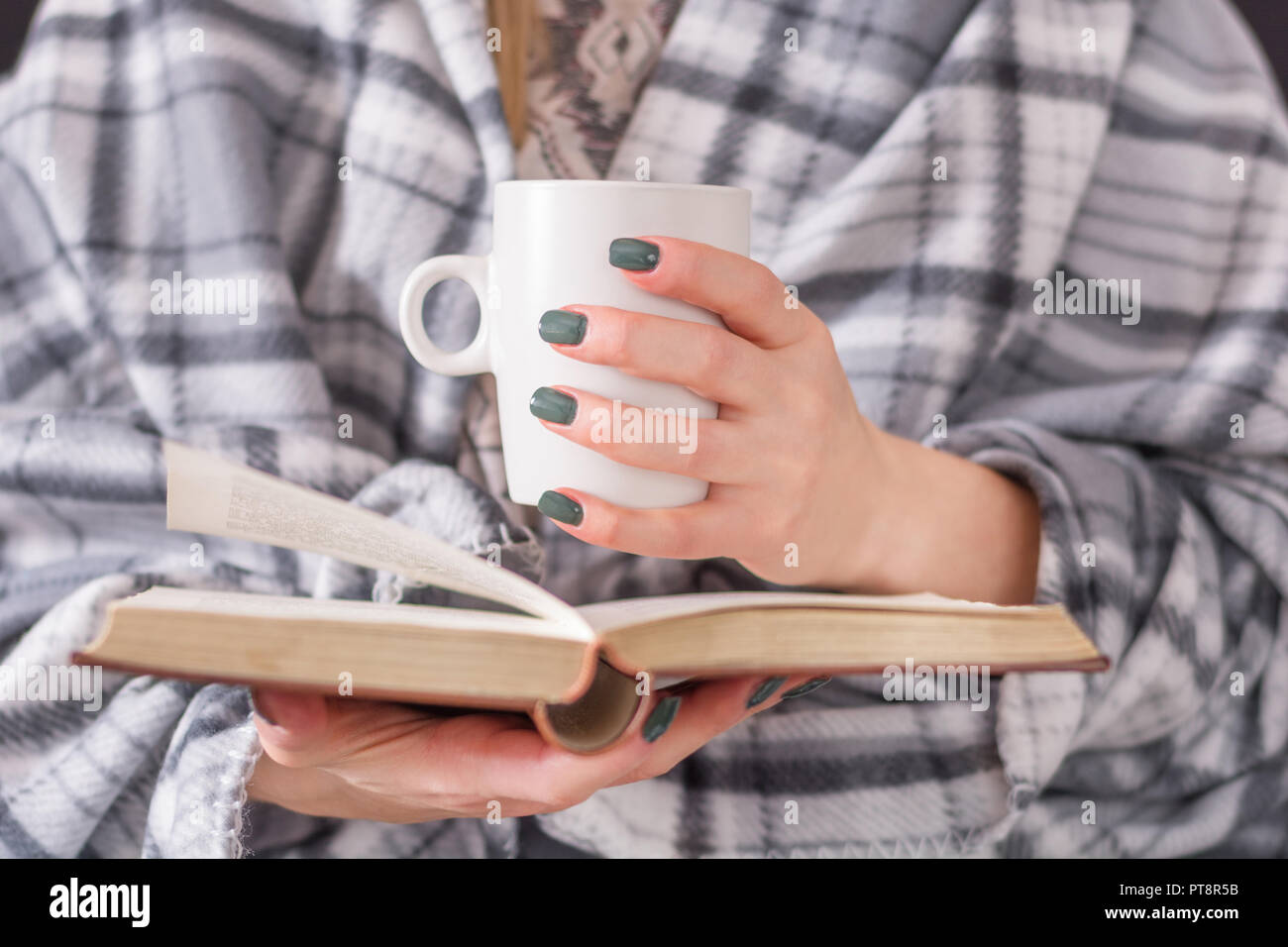 Ragazza coperto con coperta azienda prenota e la tazza di caffè e la lettura. Retrò e vintage il concetto di istruzione. Close up, il fuoco selettivo Foto Stock