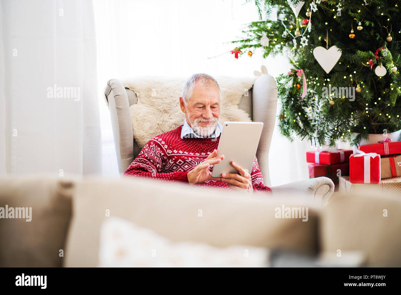 Un ritratto di uomo anziano con tavoletta seduti sulla poltrona di casa al tempo di Natale. Foto Stock