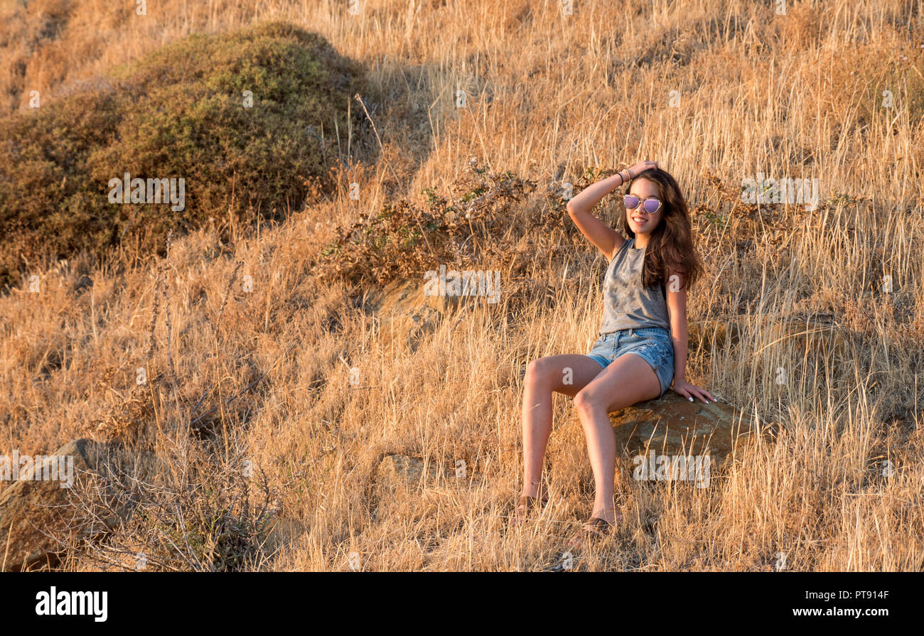 Teen in seduta pennello asciutto sul lato di una montagna di sole occhiali viola Foto Stock