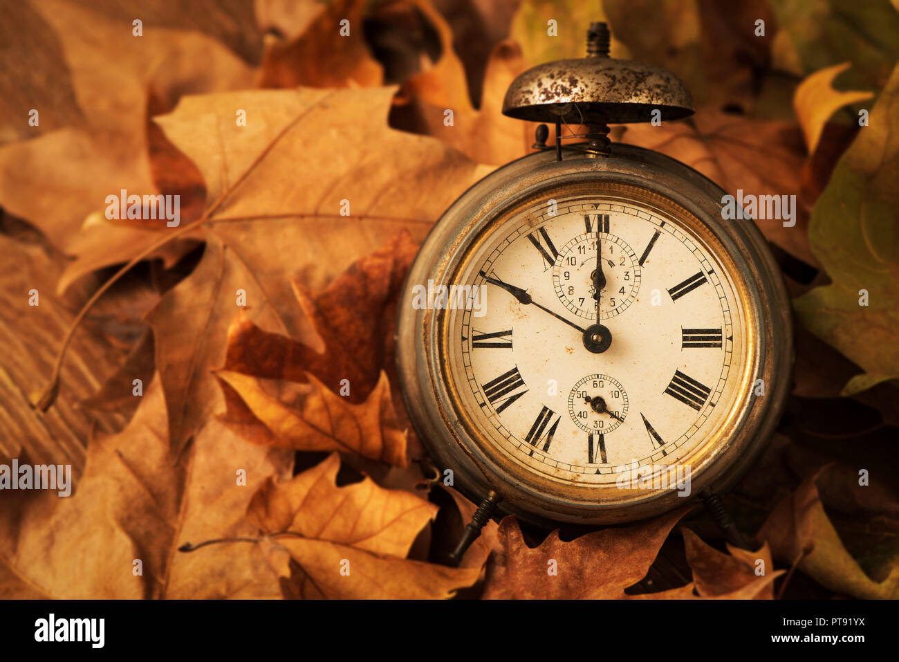 Primo piano di un vecchio e rusty sveglia circondato da foglie secche, raffigurante la fine dell'estate e l'inizio dell'autunno Foto Stock