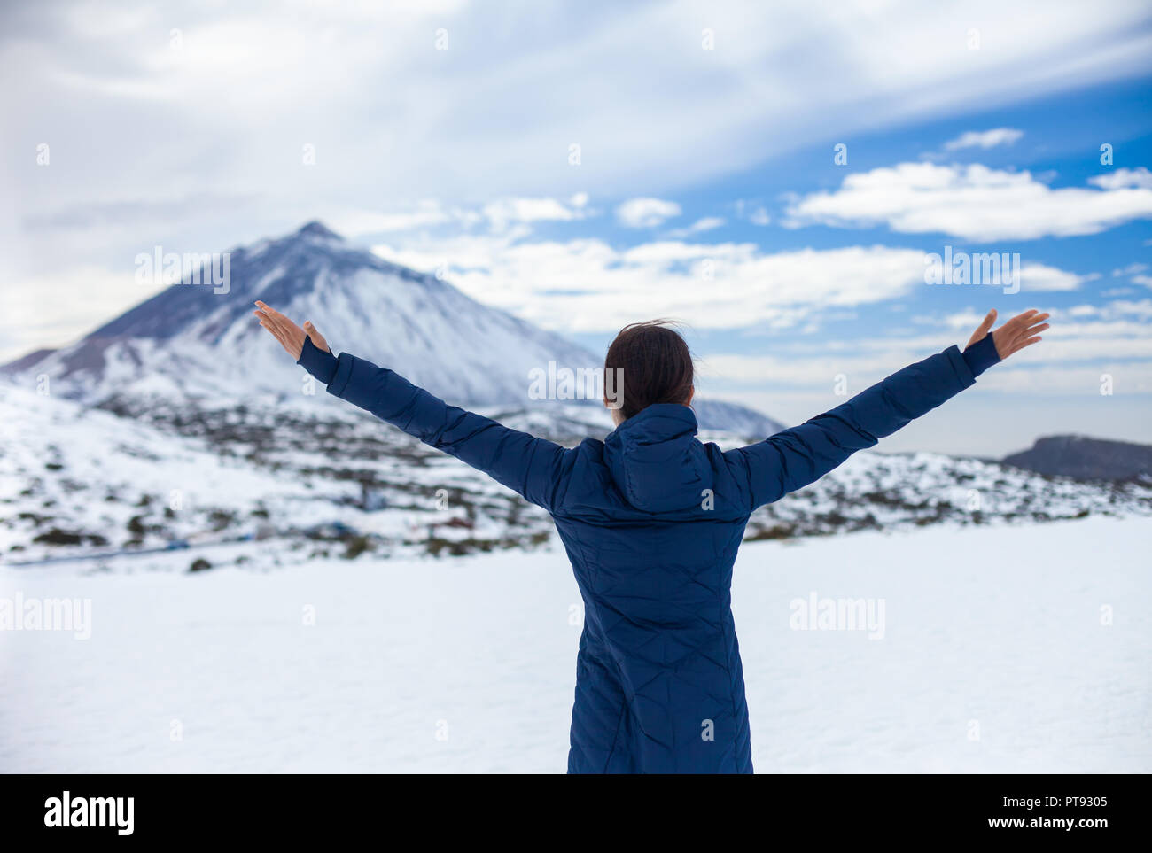 Vista posteriore della giovane donna felice con le mani fino godendo di neve montagne con vulcano El Teide sullo sfondo. Inverno in Isole Canarie Foto Stock