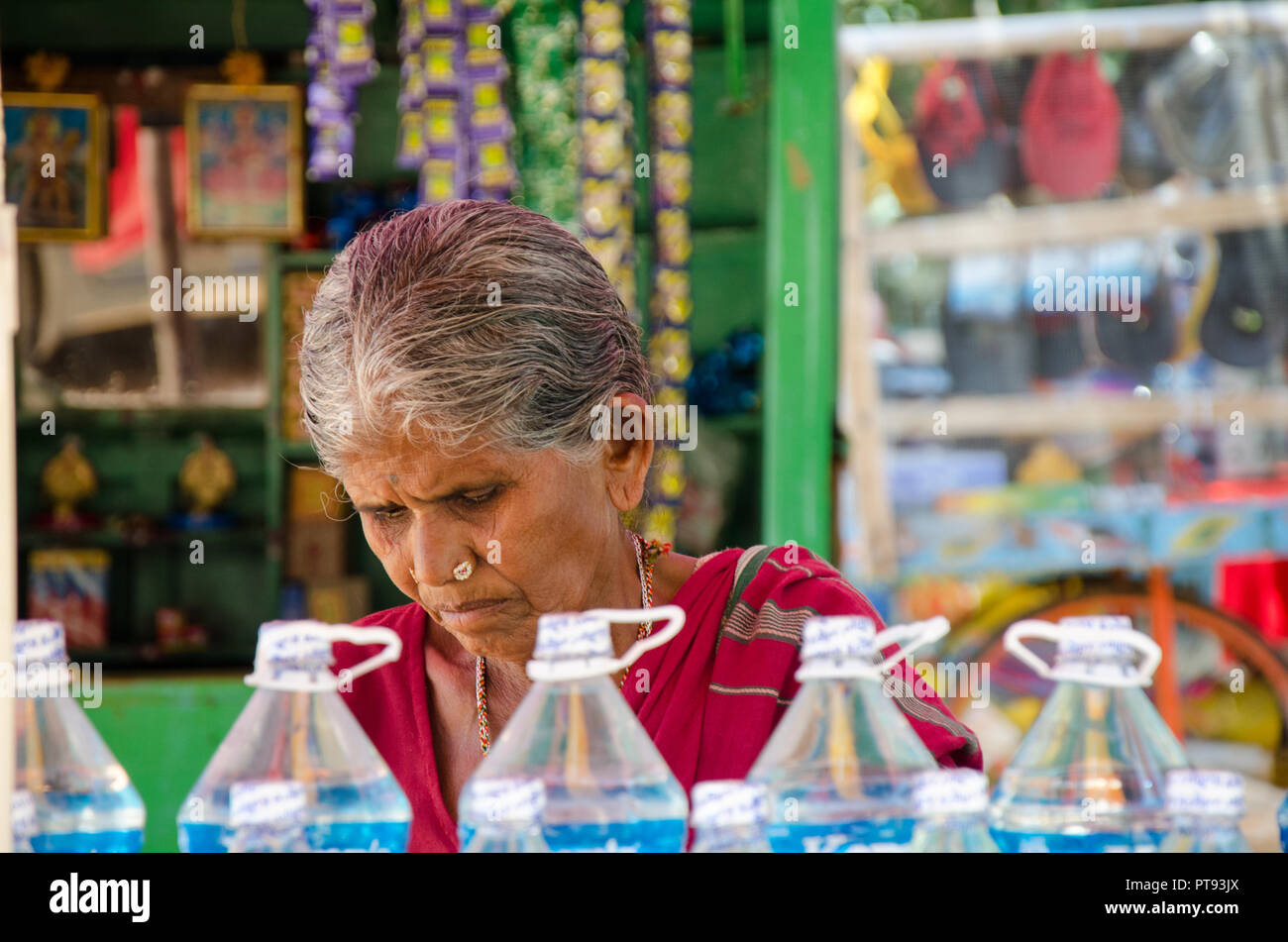 Close-up ritratto di anziani locali donna che lavorano nella sua bancarella vendendo le bottiglie di acqua e altri elementi di Hampi, Karnataka, India. Foto Stock