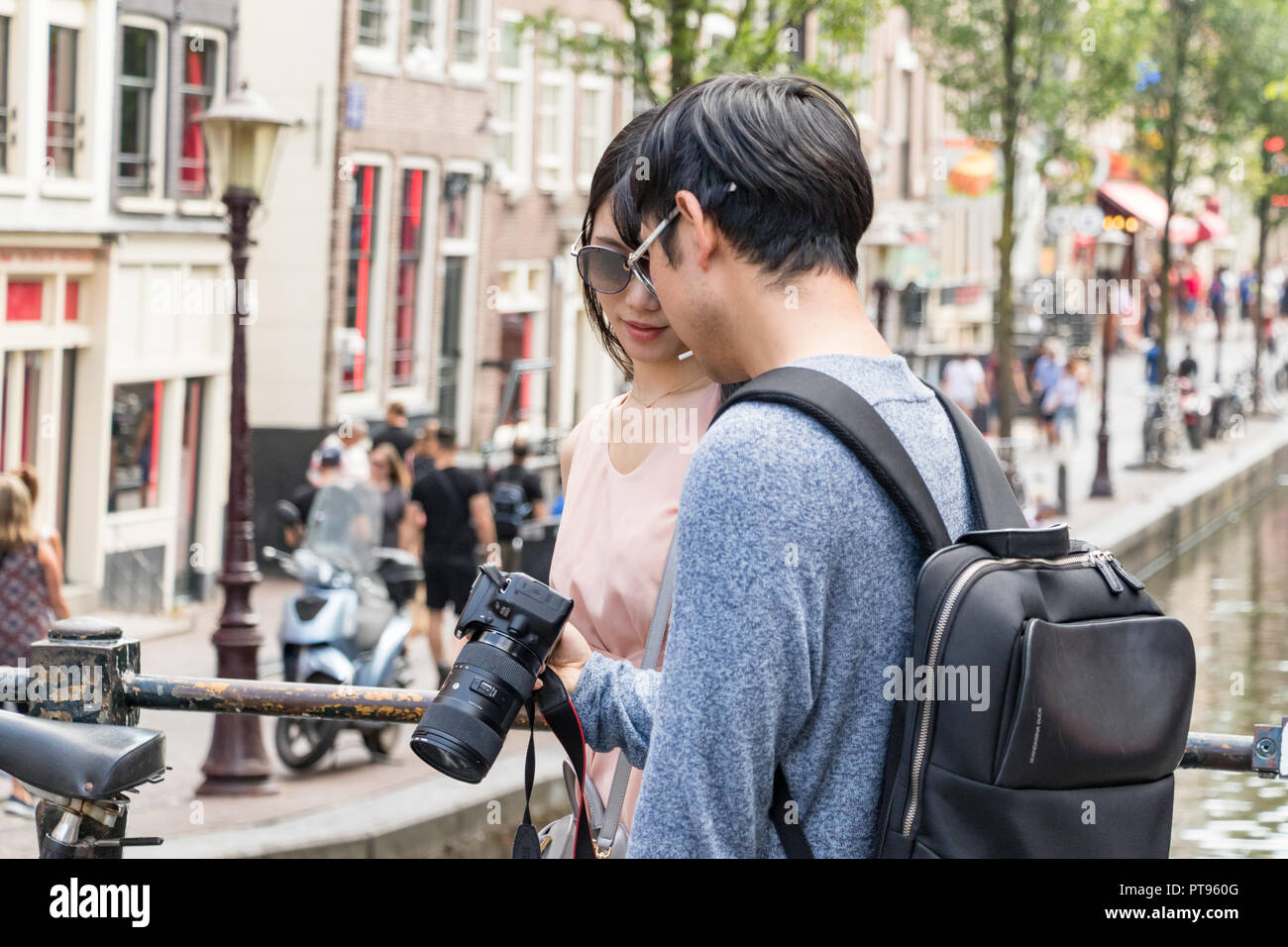 Amsterdam, Paesi Bassi, Luglio 21th, 2018: una coppia asiatica guardando le foto sulla fotocamera a piedi su un ponte presso il centro della città di Amsterdam. Foto Stock
