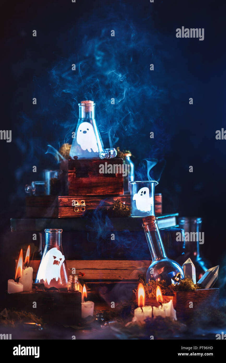 Poco fantasmi in vasetti di vetro. Concetto di Halloween su sfondo scuro con una pila di libri di magico e misterioso fumo. Foto Stock