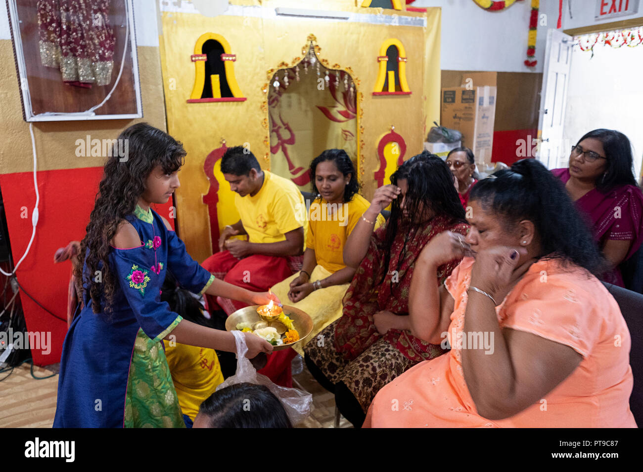 Una giovane ragazza in un sari passa per i fanatici indù con una piastra di fiori e una candela in un tempio in Richmond Hill, Queens, a New York. Foto Stock