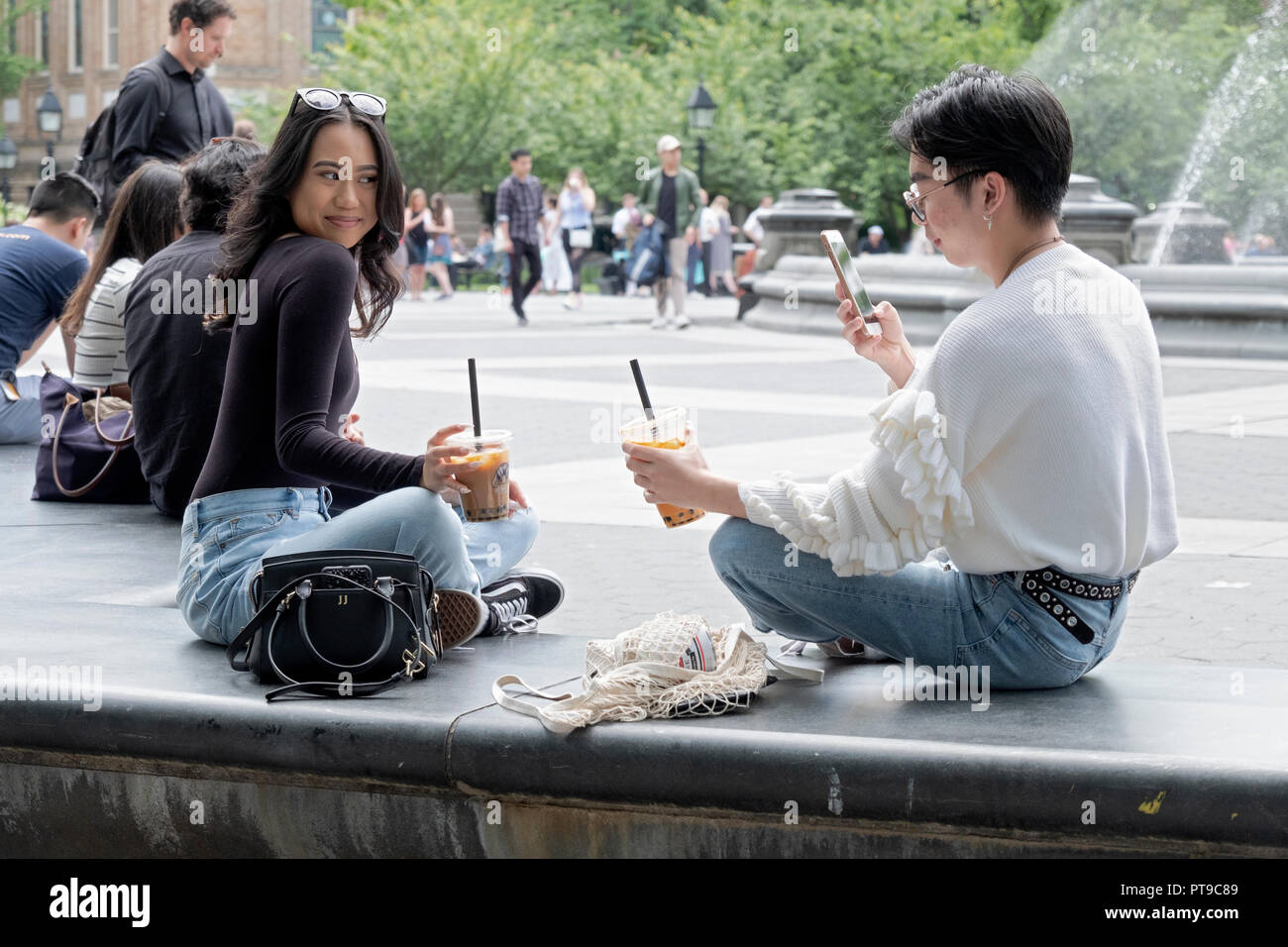 Un giovane uomo in un maglione frilly prende un telefono cellulare la foto di una bella asiatica giovane lady in Washington Square Park nel Greenwich Village di New York. Foto Stock