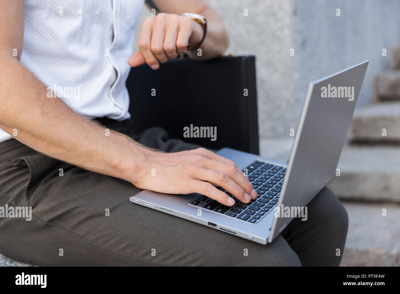 Immagine ritagliata dell uomo d affari con valigetta con computer portatile  e un orologio da polso mentre è seduto vicino alle scale Foto stock - Alamy