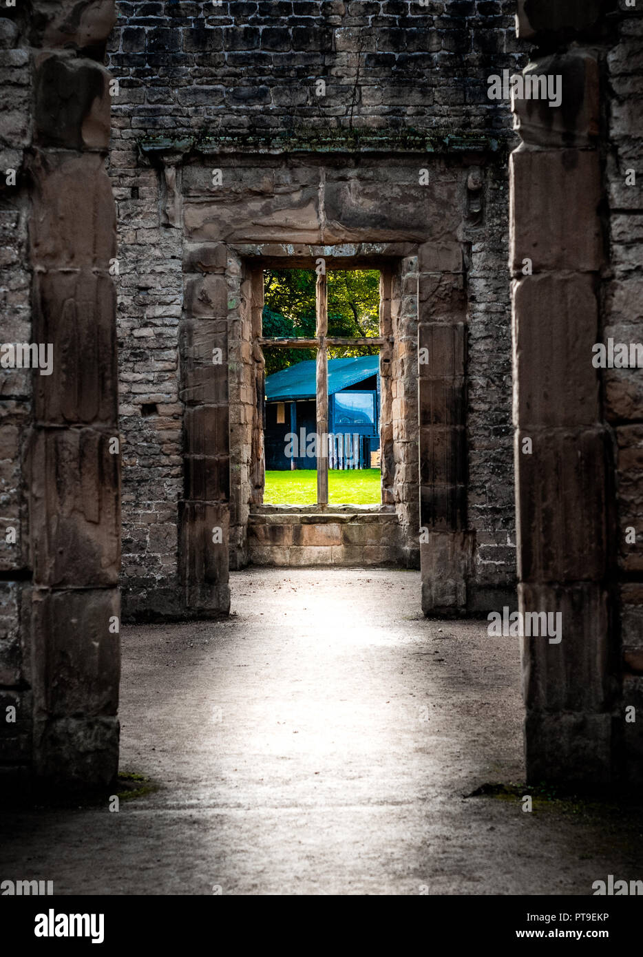 Un buio racchiuso dissaturato in corridoio che conduce ad una finestra di un paesaggio luminoso in un castello Foto Stock