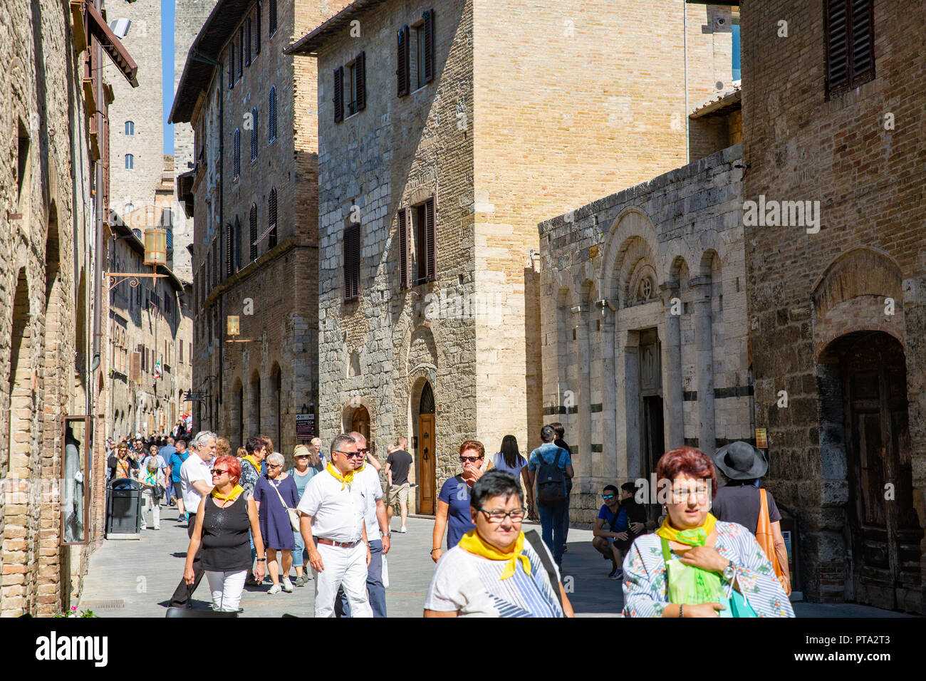 Gruppo di Tour tutti indossa foulard giallo camminato attraverso la storica cittadina collinare di San Gimignano in Toscana, a sud-ovest di Firenze,l'Italia,l'Europa Foto Stock