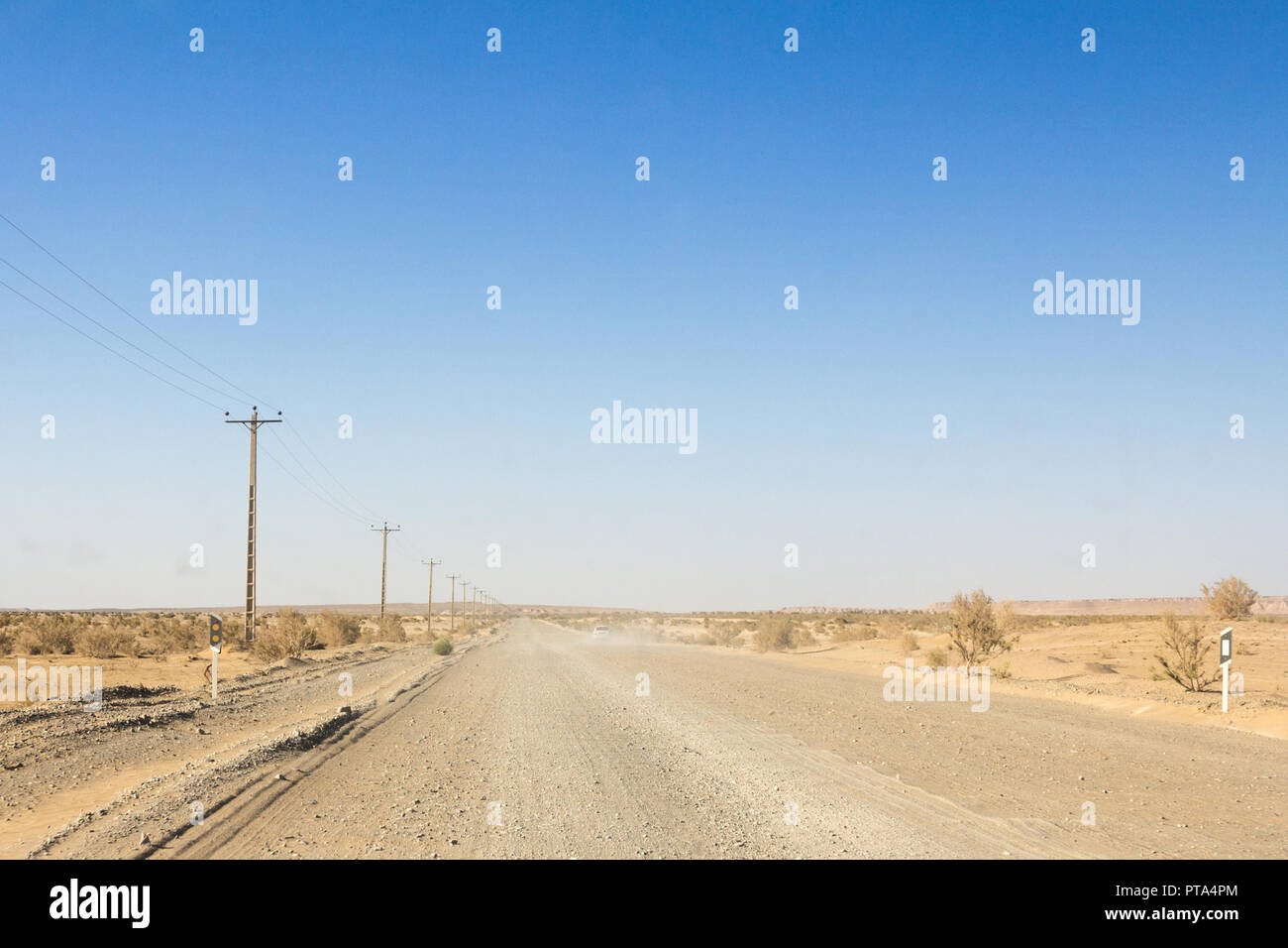 Polverosa strada nel deserto nel deserto Maranjab, in Iran, circondati da sabbia e cespugli a secco, con la forma di una vettura visibile nell'immagine di sfondo di un Foto Stock