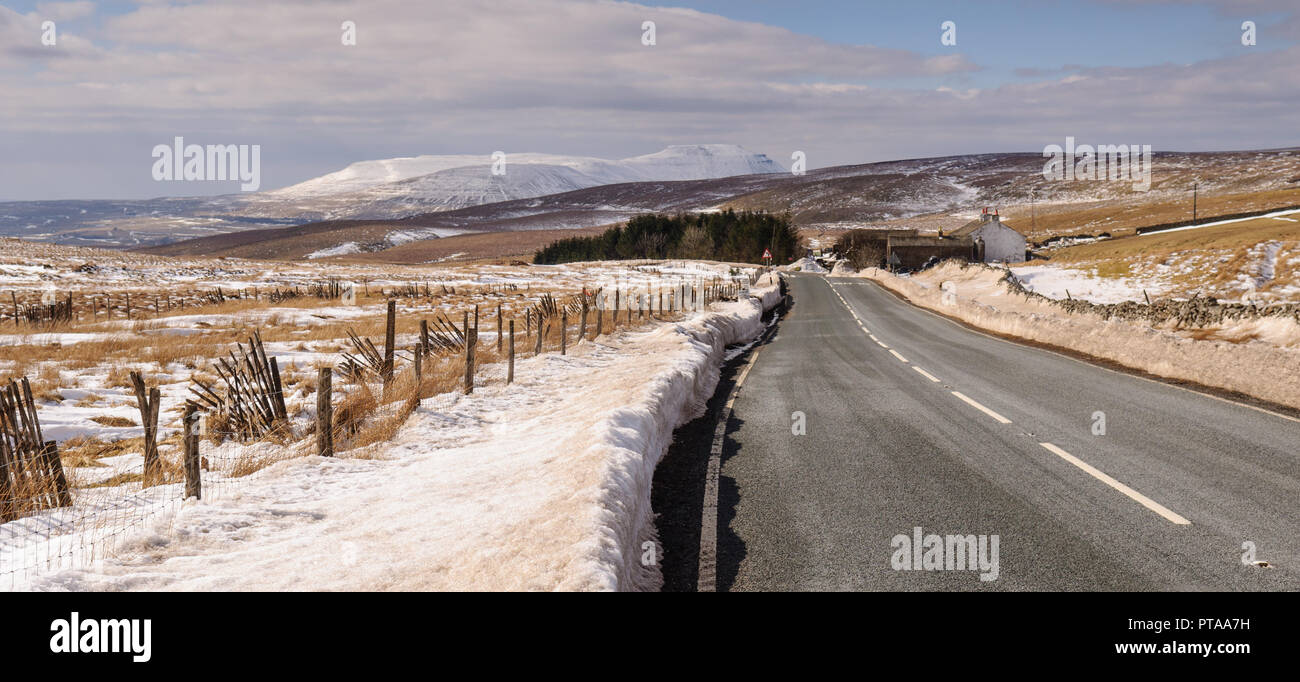 Il B6255 strada passa attraverso la neve-sparsi brughiera a Newby testa alta nel Yorkshire Dales colline, con Blea Moor Ingleborough e montagna in Foto Stock