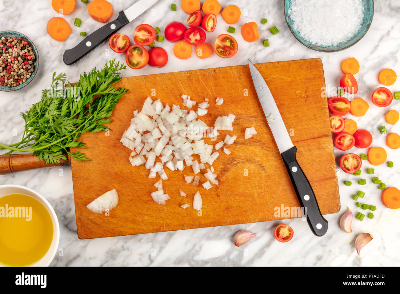 Tempo di preparazione o di mise en place. Un overhead foto professionali dei coltelli chef, ripresa dall'alto su un tagliere con un trito di verdure e spezie, su un marmo Superficie di cottura Foto Stock