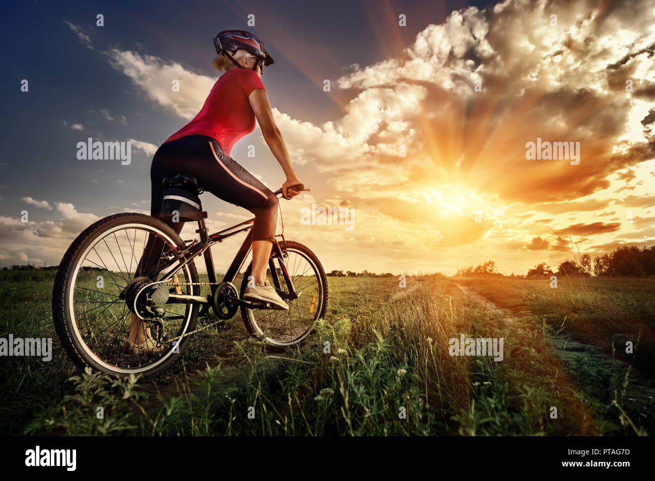 Ragazza sportive su una bicicletta guardando il tramonto alla fine della strada. Il concetto di libertà di viaggio, il movimento verso l'obiettivo. Tonificazione. Foto Stock