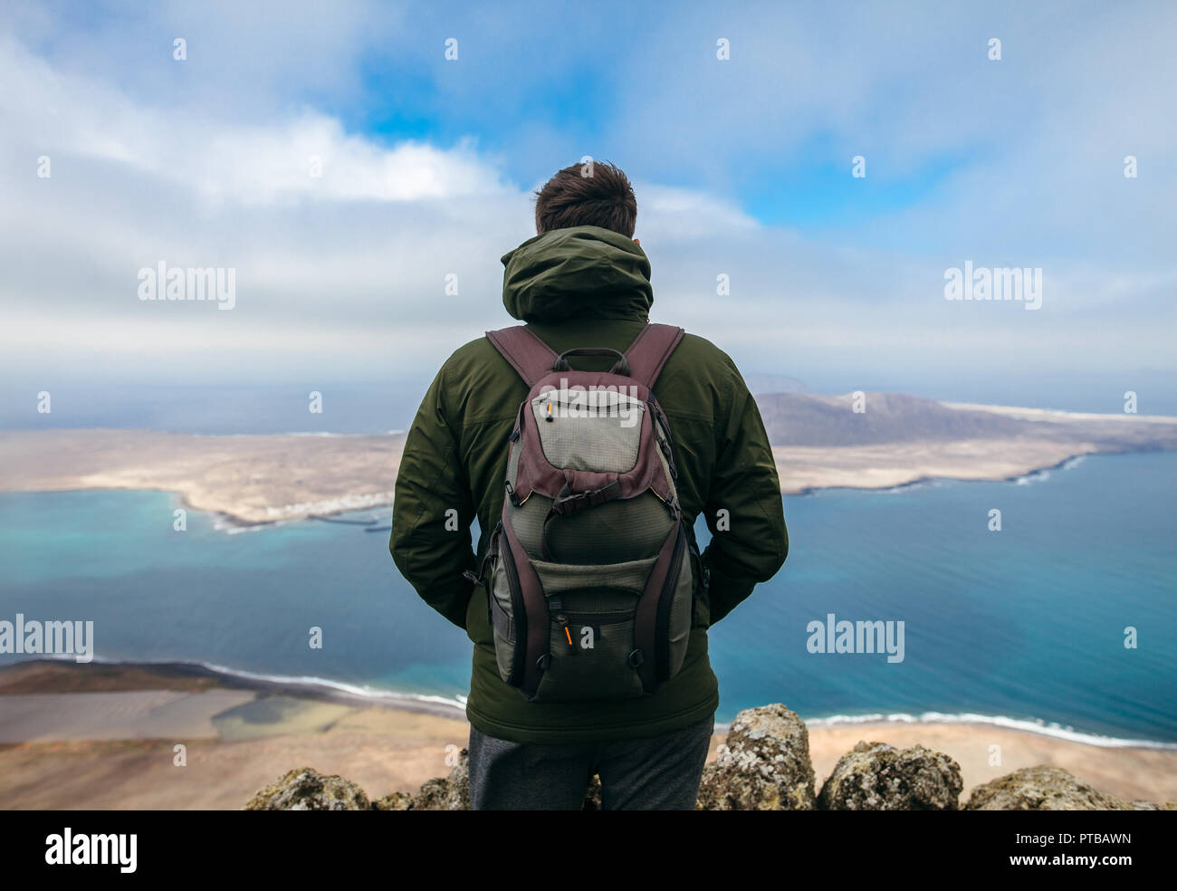 Vista posteriore del viaggiatore uomo godendo di bellissimi paesaggi marini di La Graciosa isola a Viewpoint. Concetto di viaggio. Inverno in Isole Canarie Foto Stock
