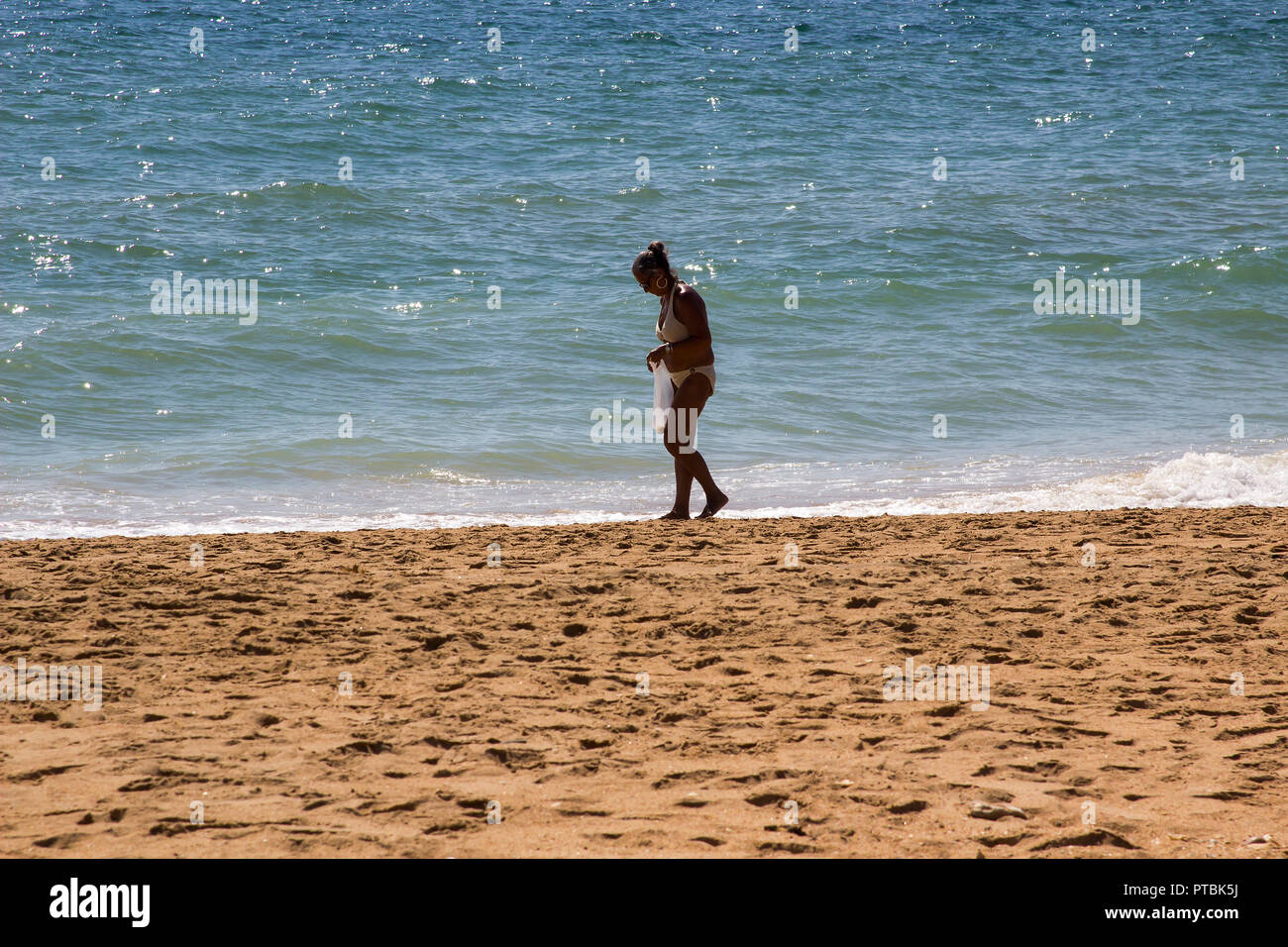 28 settembre 2018 una femmina solitaria in un bikini raccogliendo conchiglie e pietre su una sabbiosa spiaggia Praia do spiaggia Inatel Albuferia in Algave Portogallo Foto Stock