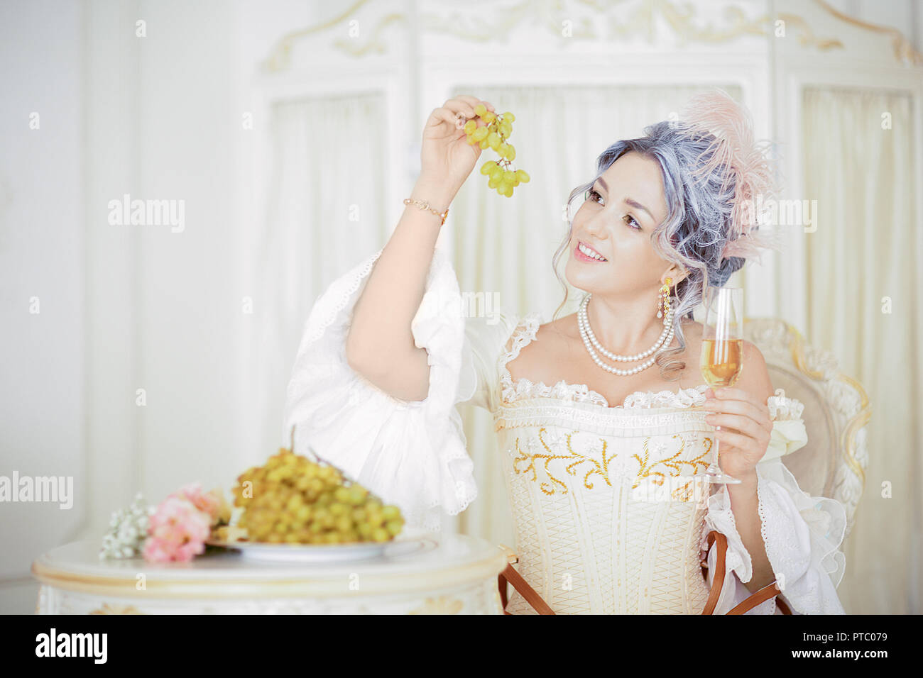 Bella donna grayhead in abito rococò in posa di fronte di sfondo storico  mentre mangia l'uva. Studio fotografico. halloween Foto stock - Alamy