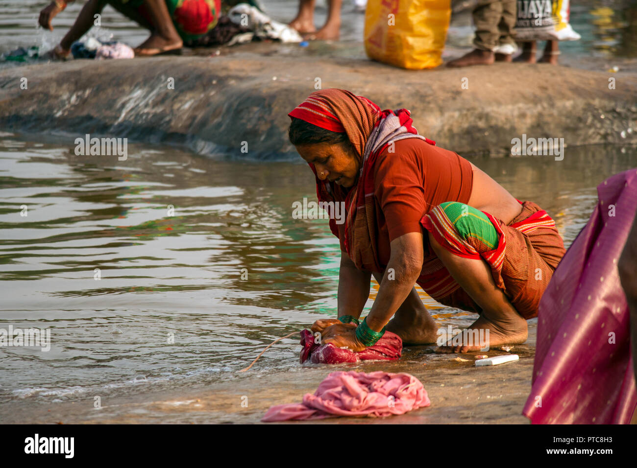 Un vestito tradizionale eldery donna conduce la sua routine quotidiana di lavaggio a mano i suoi familys vestiti sulla roccia rive del fiume Tungabhadra, Hambi, Foto Stock