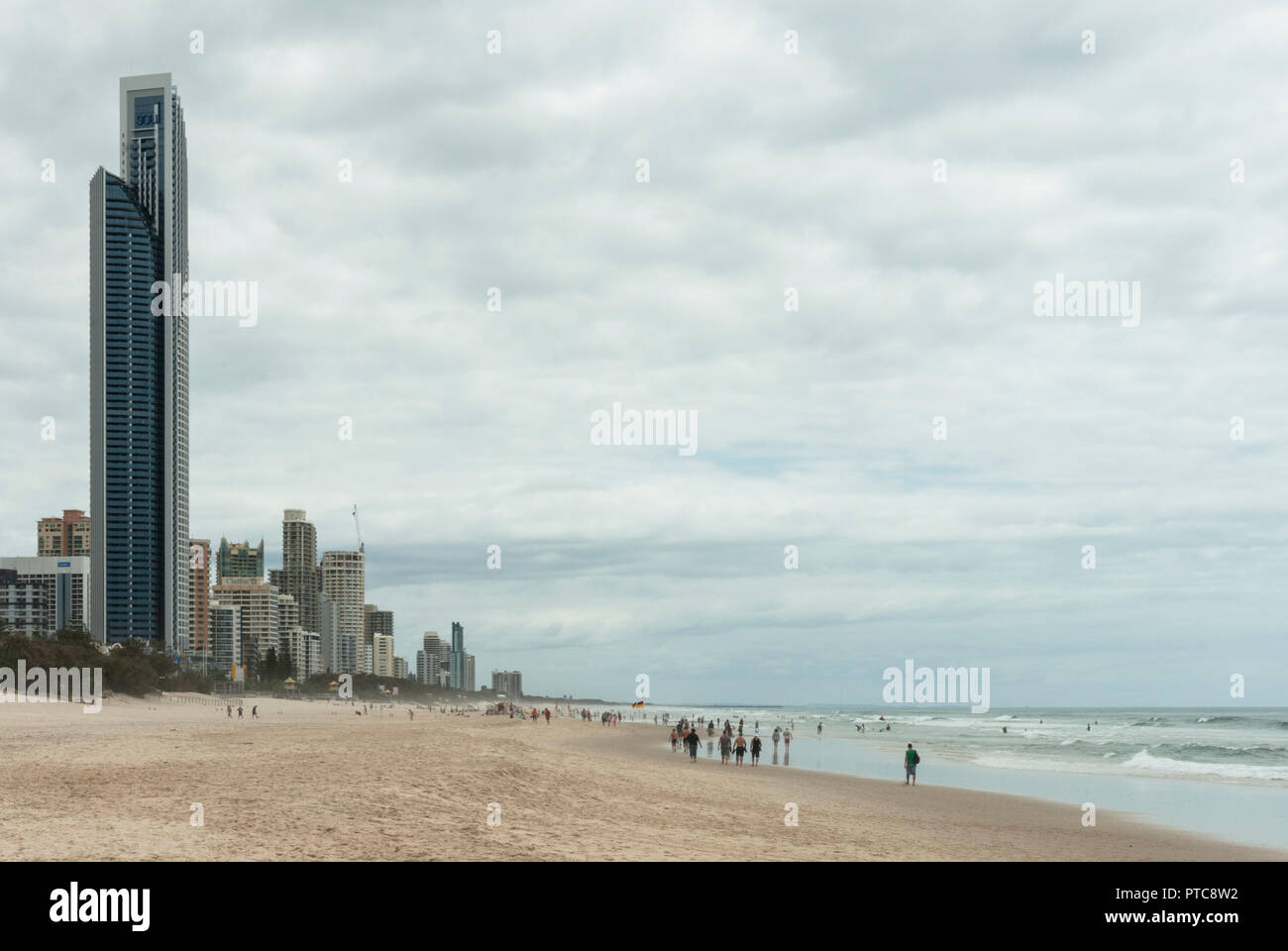 Vista lungo di Surfers Paradise beach con sabbia, mare, Anima Tower e nella distanza persone che passeggiano a bordo delle acque. Foto Stock