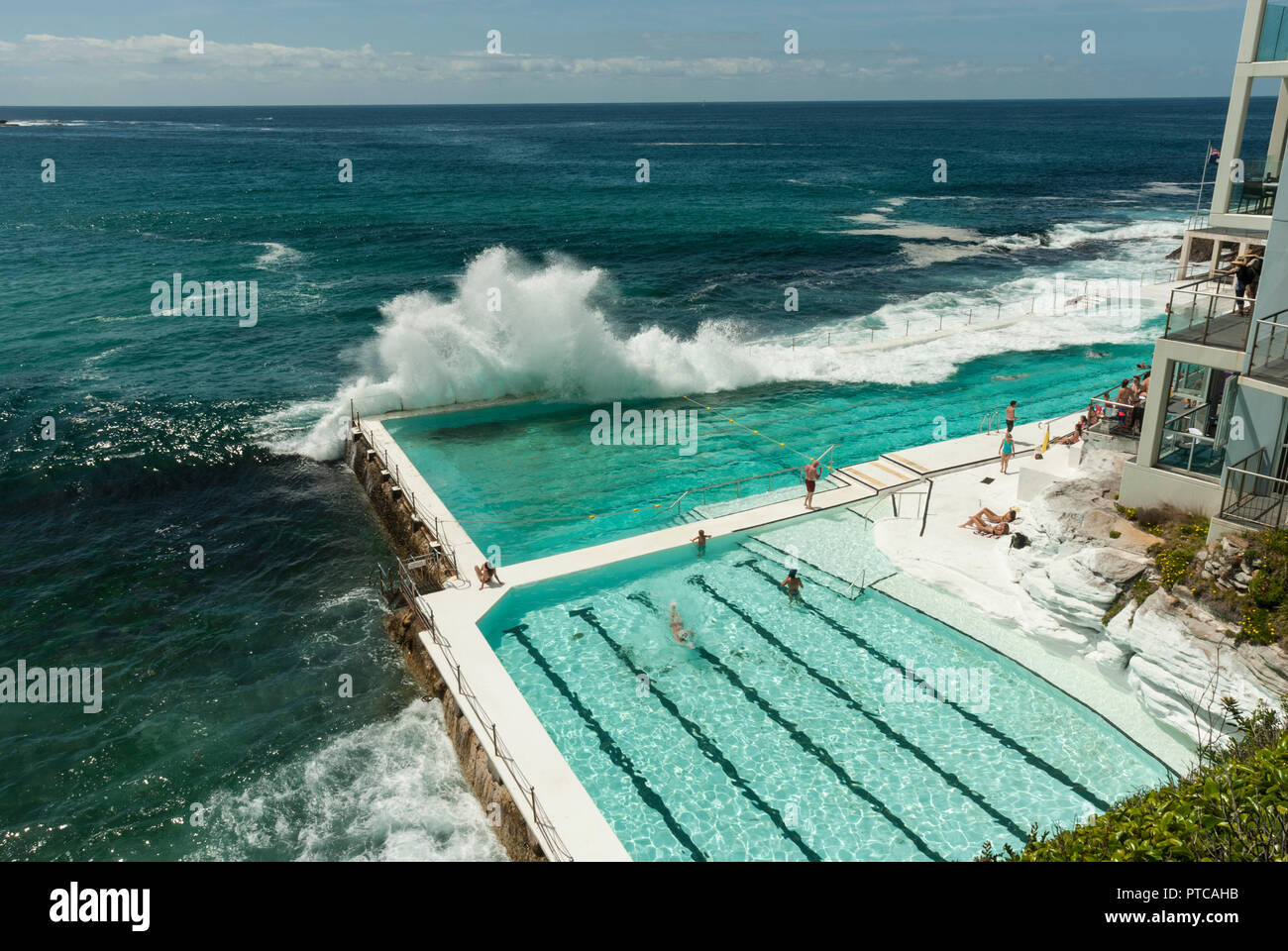 Onde enormi cascading su Bondi Iceberg acqua di mare piscine esterne (Sydney). Sole e attraente verde blu piscine con alcune persone in piscina. Foto Stock