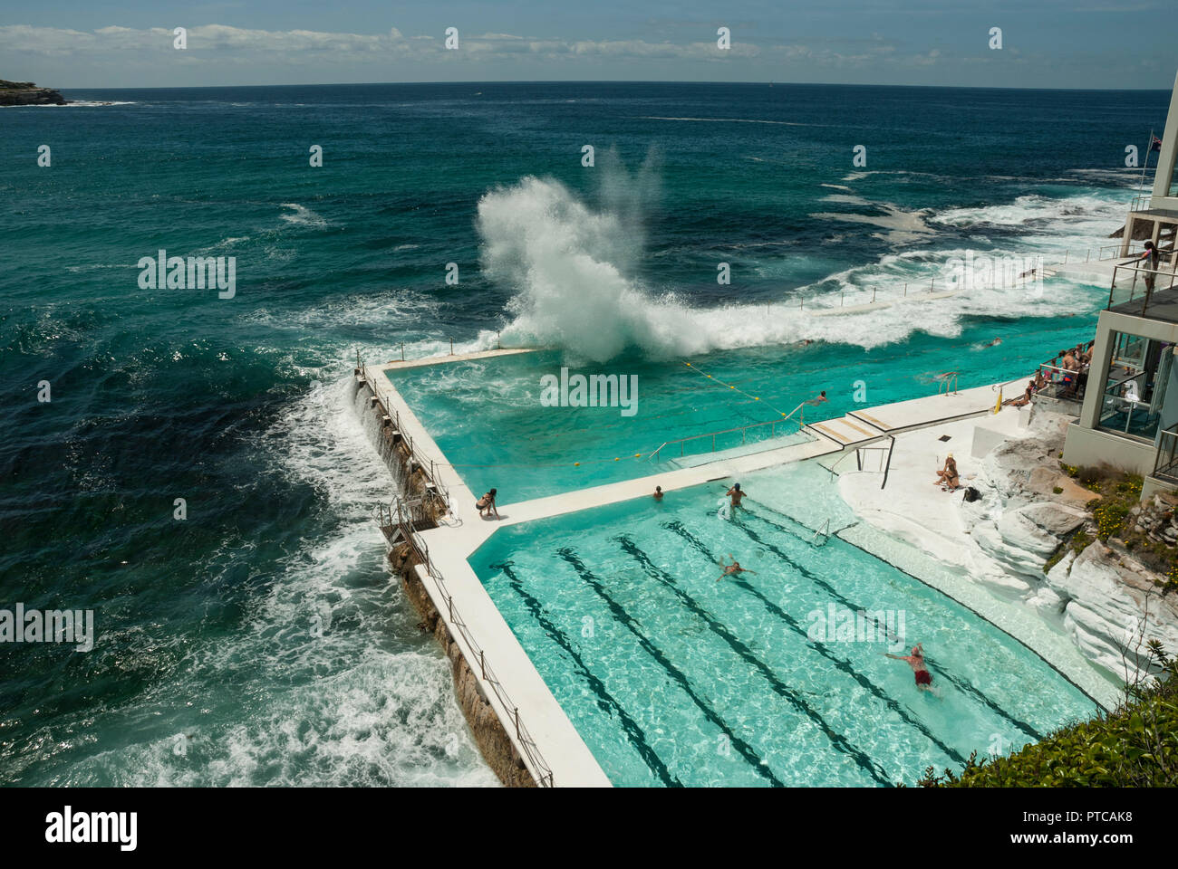 Onde enormi cascading su Bondi Iceberg acqua di mare piscine esterne (Sydney). Sole e attraente verde blu piscine con alcune persone in piscina. Foto Stock