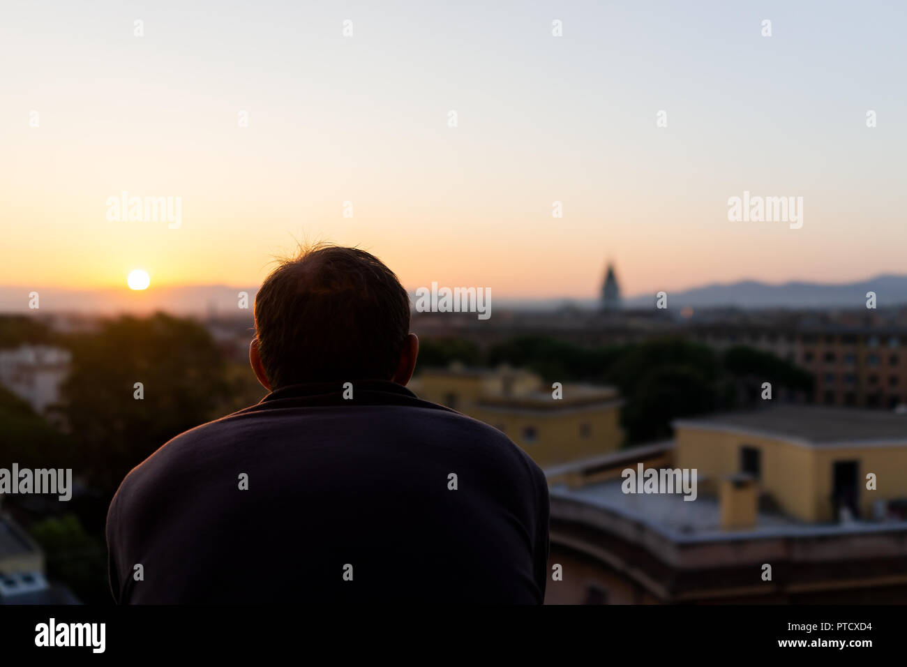 Retro del giovane uomo a guardare il tramonto in Italia a Roma città storica con il campanile di una chiesa, serata estiva tramonto notte cityscape skyline, mountain vista aerea Foto Stock