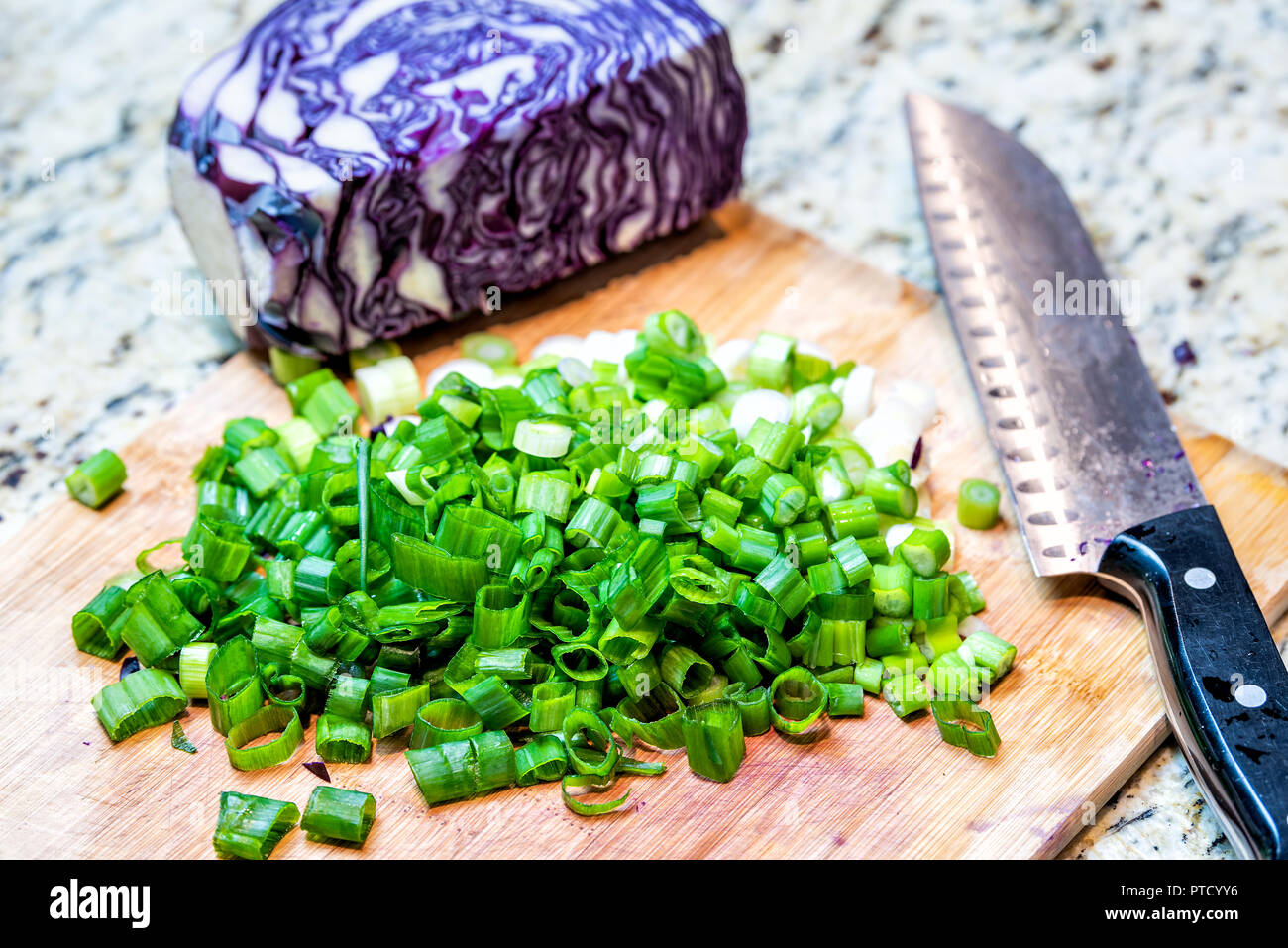 Tagliere, viola, cavolo rosso, di scalogni tagliati a fette, tagliare il cipollotto, coltello in cucina sul piano del banco in granito con nessuno durante la cottura e la preparazione di foo Foto Stock