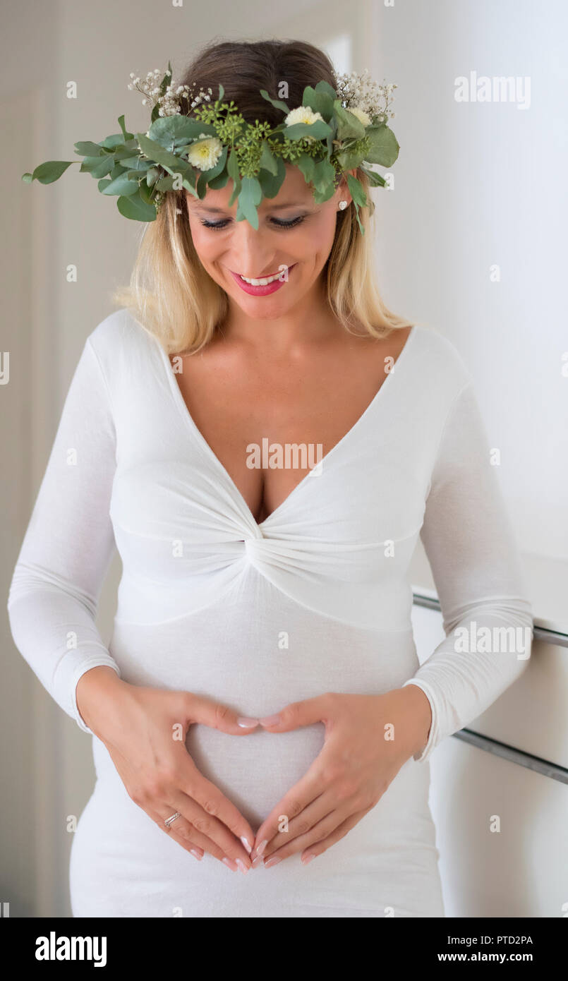 Donna, sposa, con corona di fiori, nove mesi di gravidanza, con le mani formando un cuore di fronte la sua gravidanza ventre, Germania Foto Stock