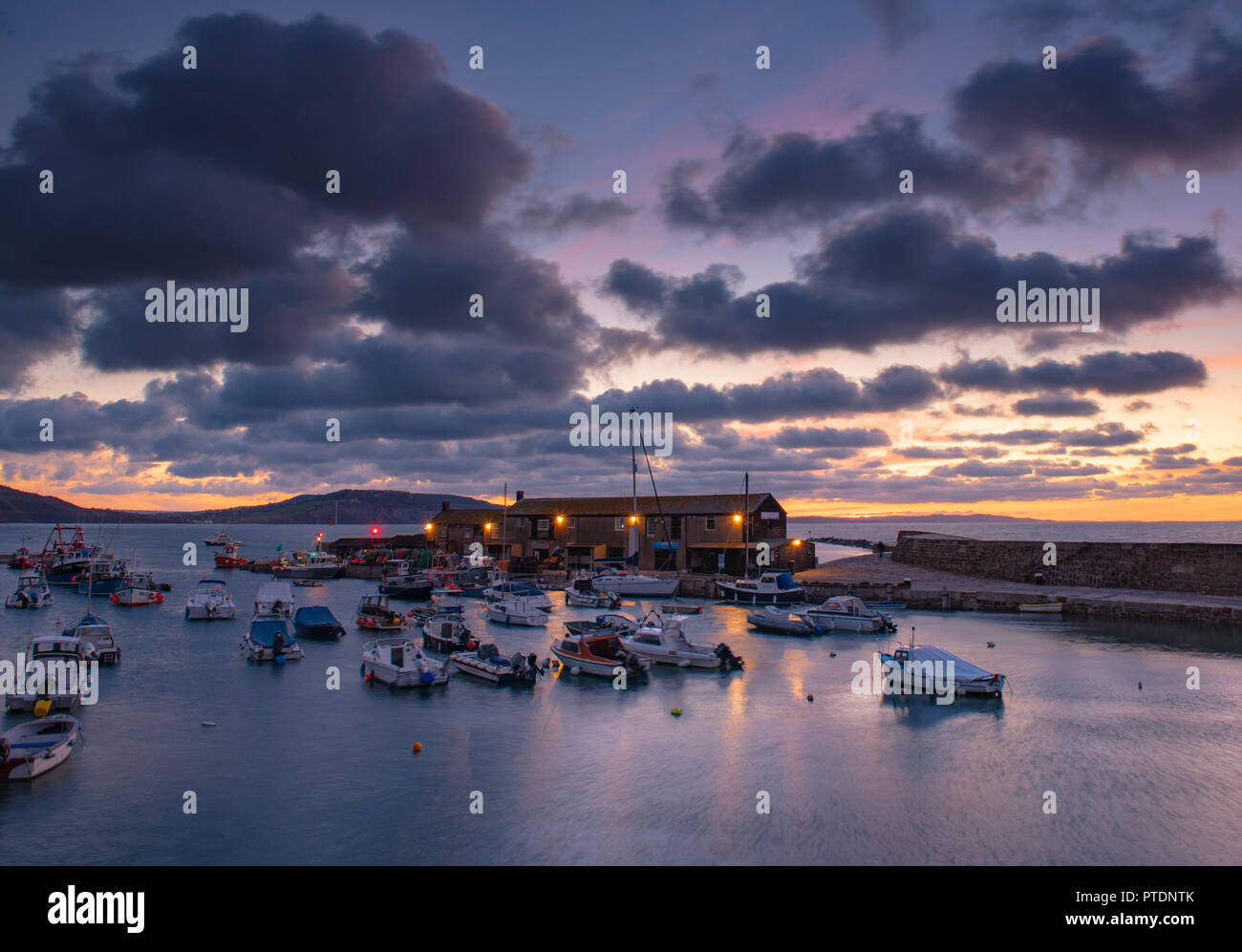 Lyme Regis, Dorset, Regno Unito. Il 9 ottobre 2018. Regno Unito Meteo: Moody mattina nuvole come sunrise colori illuminano il cielo sopra il Cobb, Lyme Regis. Credito: Celia McMahon/Alamy Live News Foto Stock