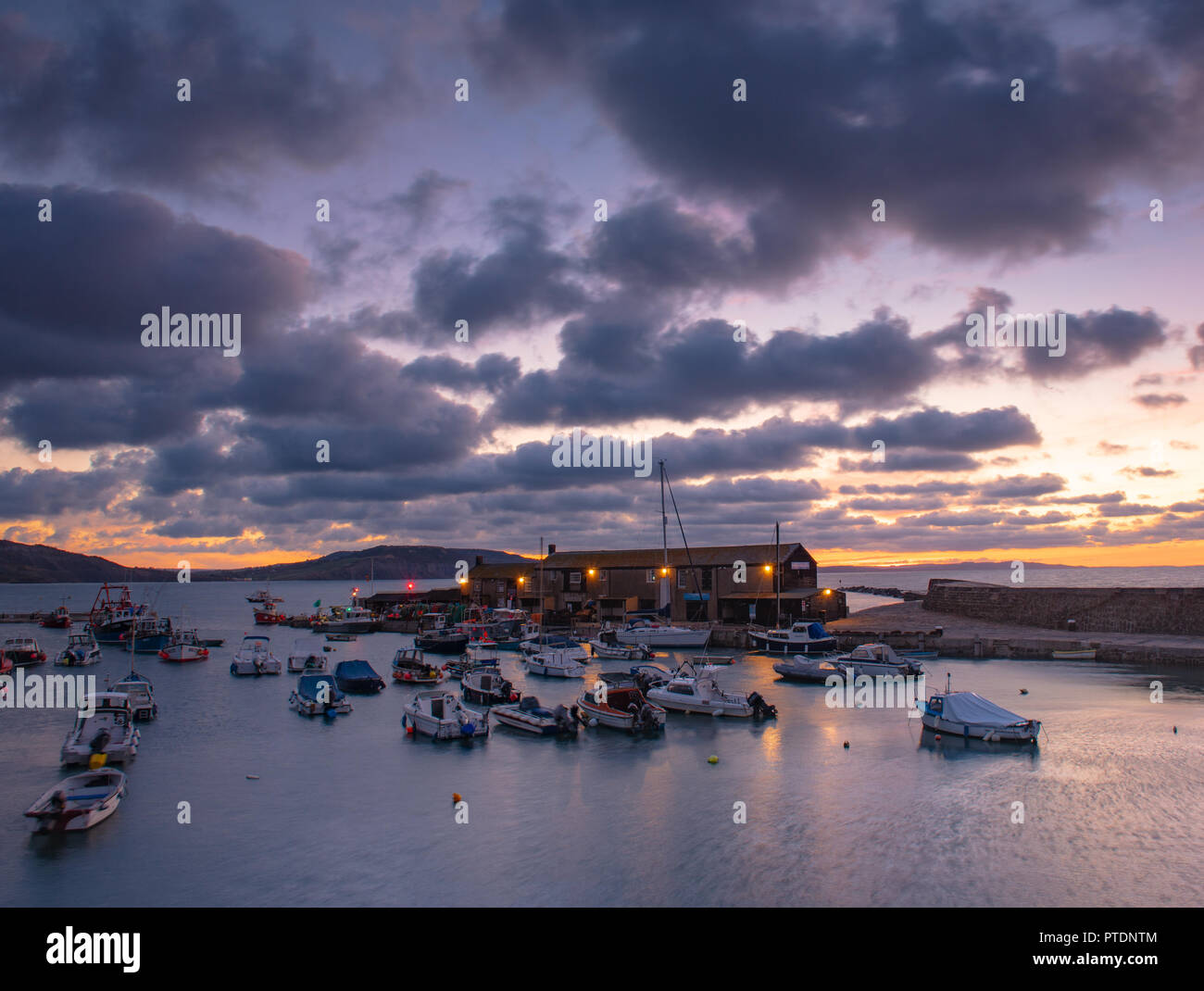 Lyme Regis, Dorset, Regno Unito. Il 9 ottobre 2018. Regno Unito Meteo: Moody mattina nuvole come sunrise colori illuminano il cielo sopra il Cobb, Lyme Regis. Credito: Celia McMahon/Alamy Live News Foto Stock