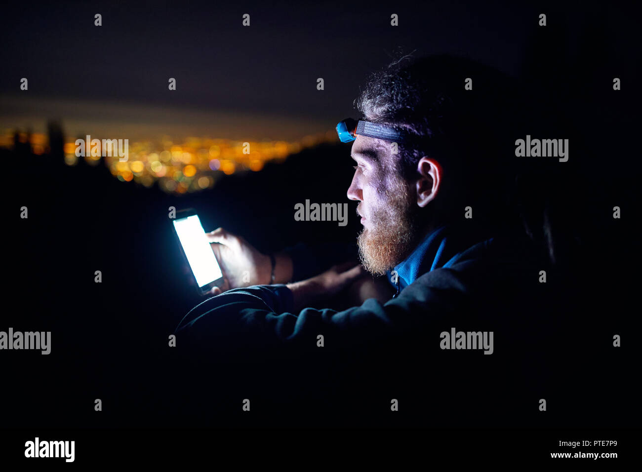 Ritratto di uomo con smartphone incandescente e luci led contro il cielo notturno con stelle e incandescente città sfondo luminoso. Foto Stock