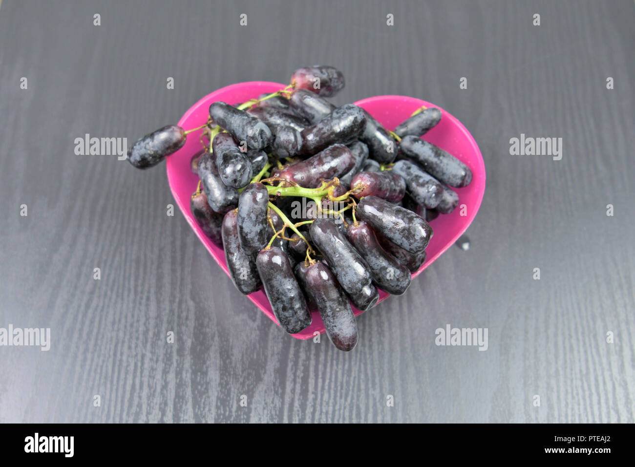 Lungo l'uva nera in un cuore rosa Ciotola sagomata Foto Stock