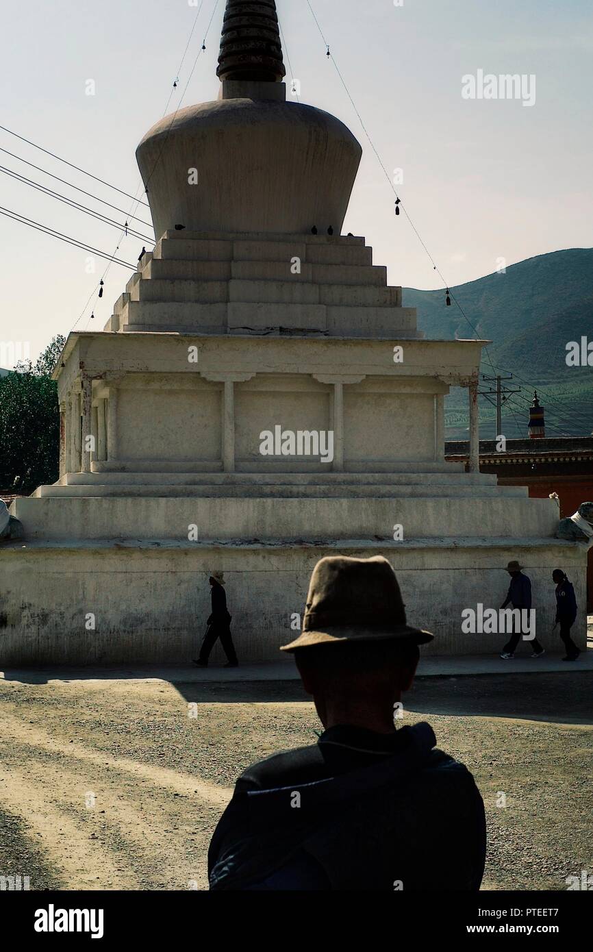 Monastero di Labrang, Xiahe, provincia di Gansu / Cina - 6 GIU 2011: buddista tibetana pellegrini a piedi attorno a uno stupa mentre un uomo in un tradizionale hat watch Foto Stock