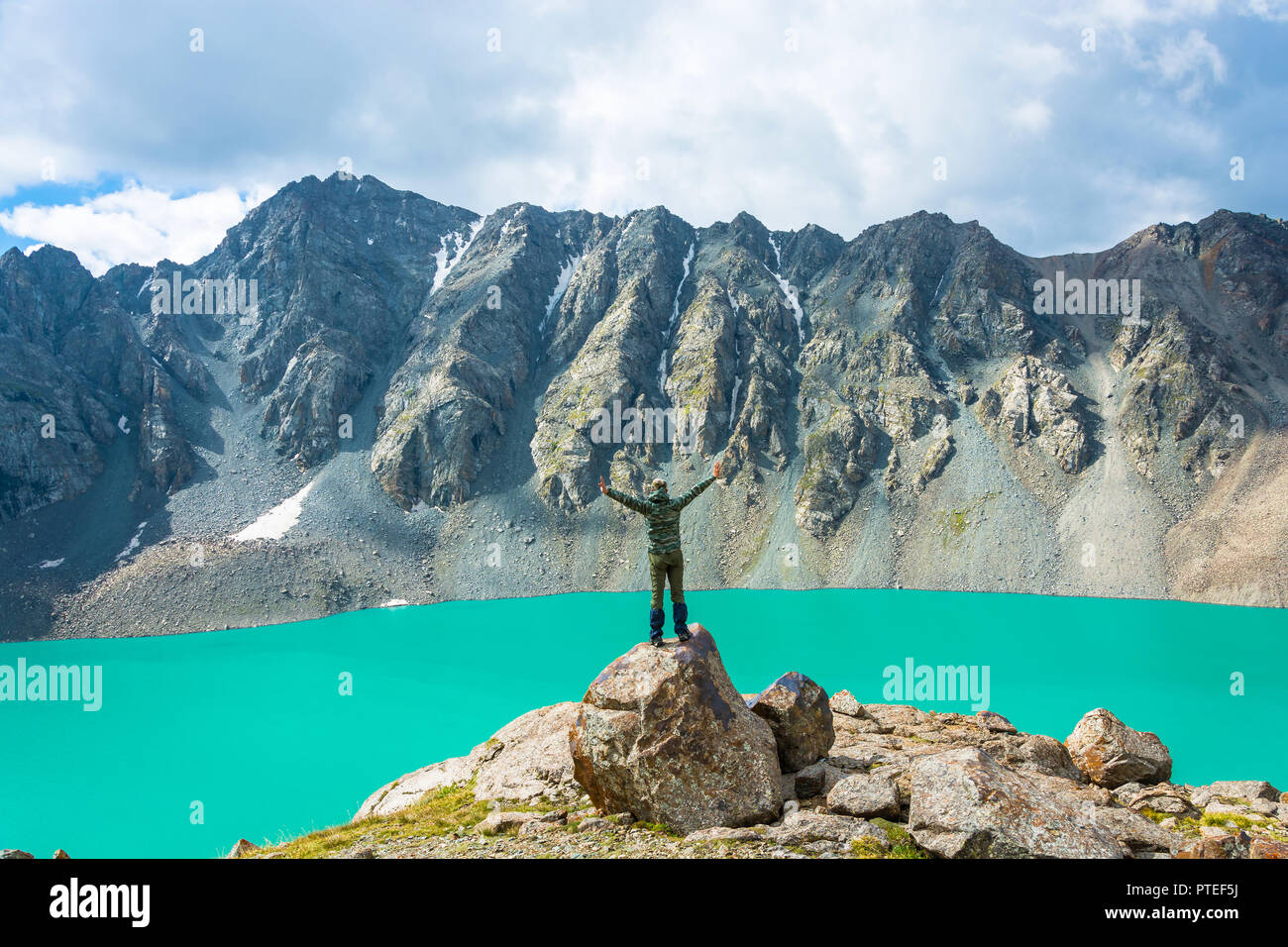 Un uomo in piedi su un enorme roccia esegue le asana sullo sfondo di un lago di montagna Ala-Kul, Kirghizistan. Foto Stock
