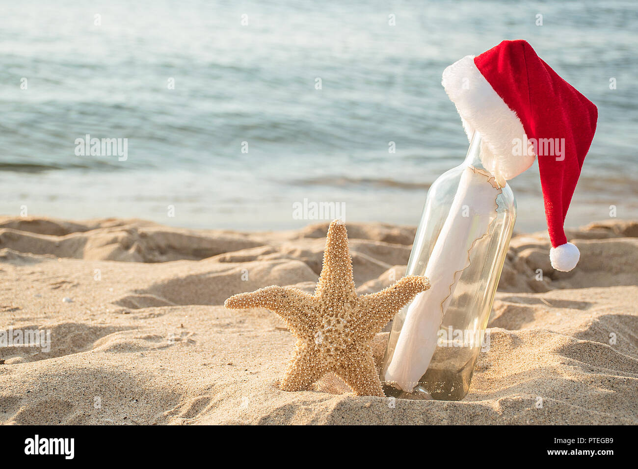 Santa hat su un messaggio in bottiglia con stella di mare nella spiaggia di sabbia e fondo di acqua Foto Stock