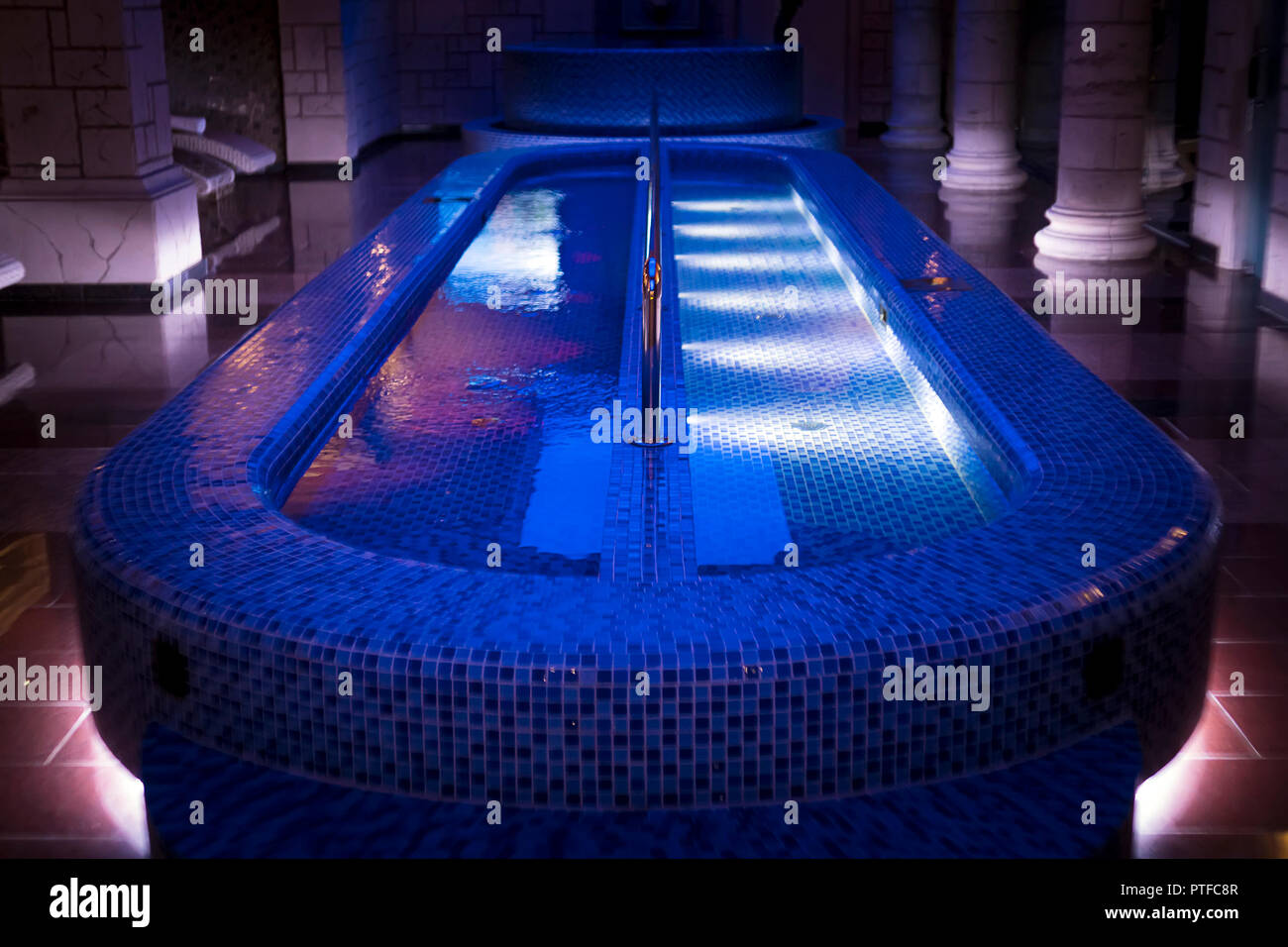 Un lusso pillared spa hall con gli illuminati piscina a tuffo nel centro. Un vuoto che la bella blu-piastrellate piscina spa dell'hotel deluxe. Colonne di parete sa Foto Stock