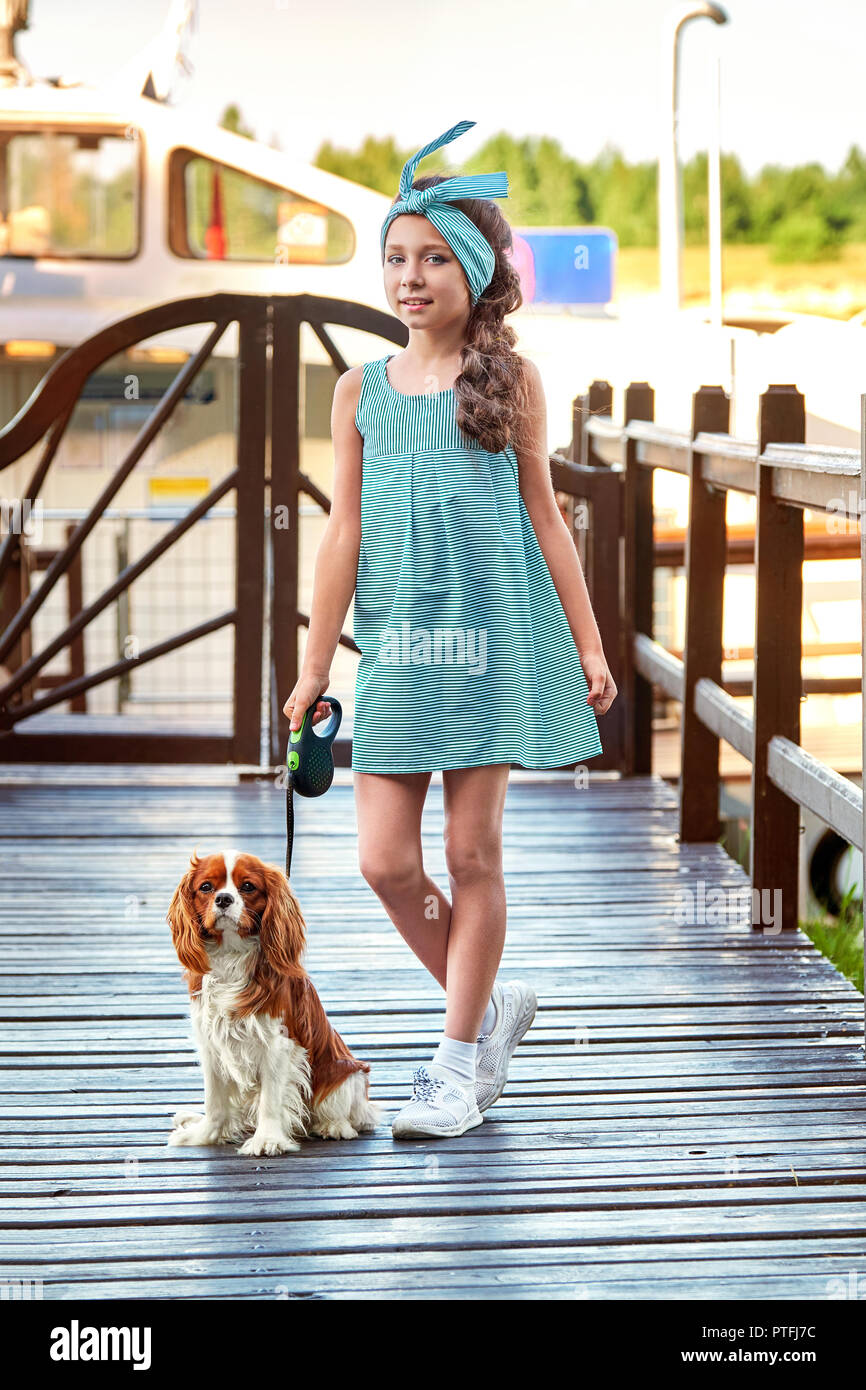 Elegante bambino nei pressi di cucciolo di razza cocker spaniel,charles king.giovane e bella ragazza sta molo ponte. Signora della vogue,blue striped dress,stile marina,cruise,l'estate.Designer Collection.Kid Fashion Concept. Foto Stock