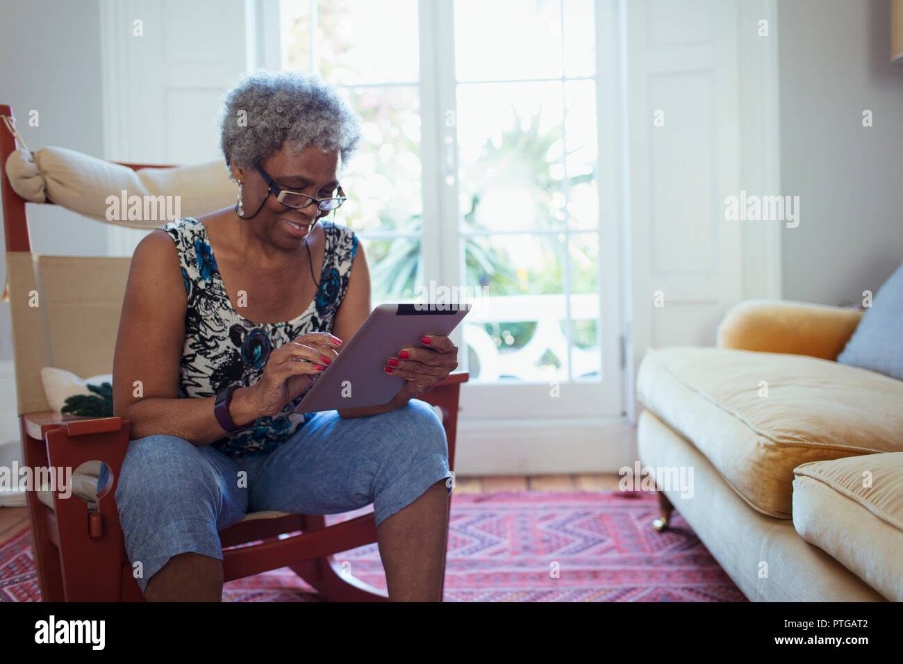 Donna senior con tavoletta digitale in salotto Foto Stock