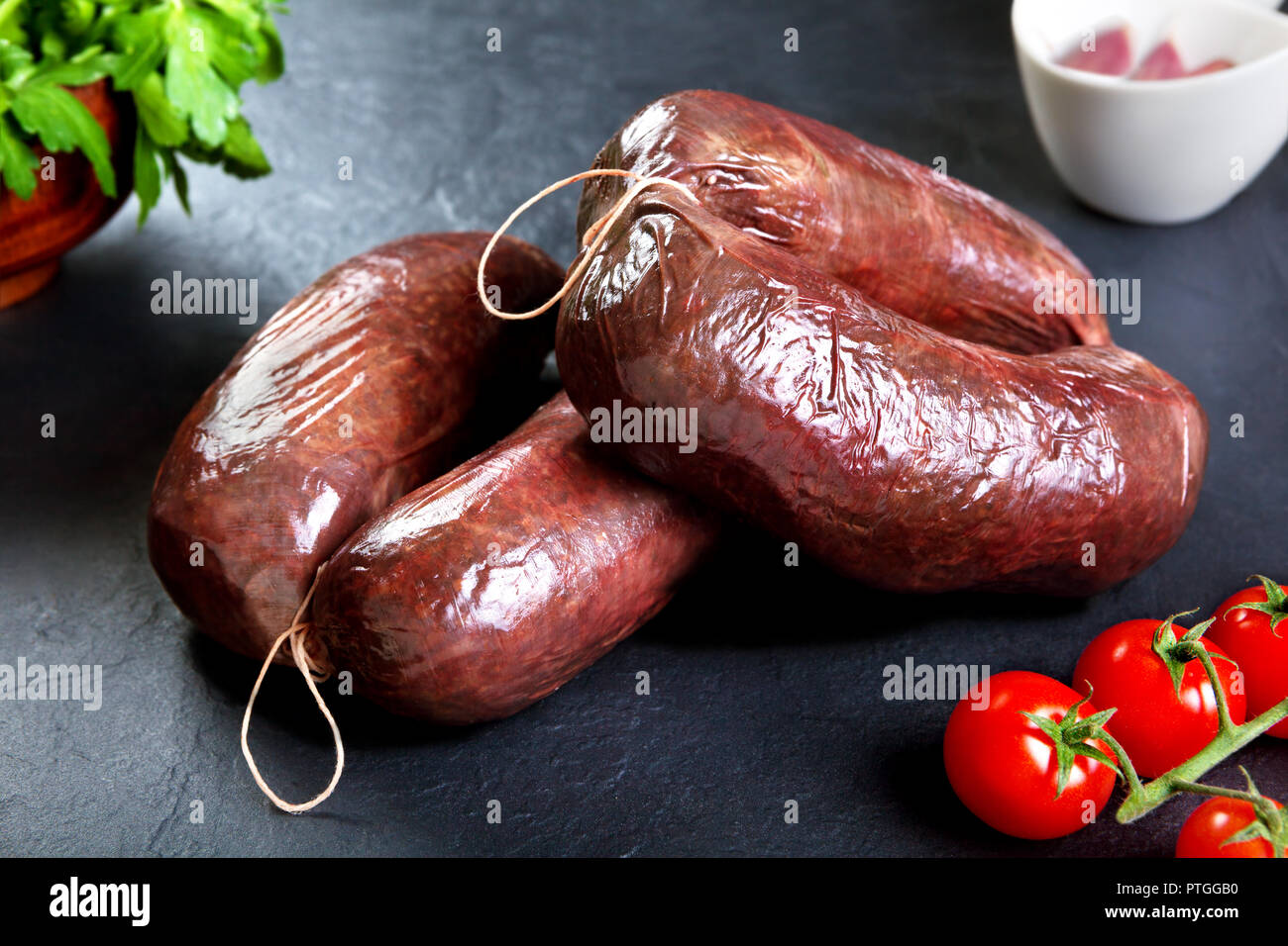 Non cotte fresche salsicce di sangue con il prezzemolo e il pomodoro. carne di maiale cruda pronto a cuocere in pietra nera sullo sfondo Foto Stock