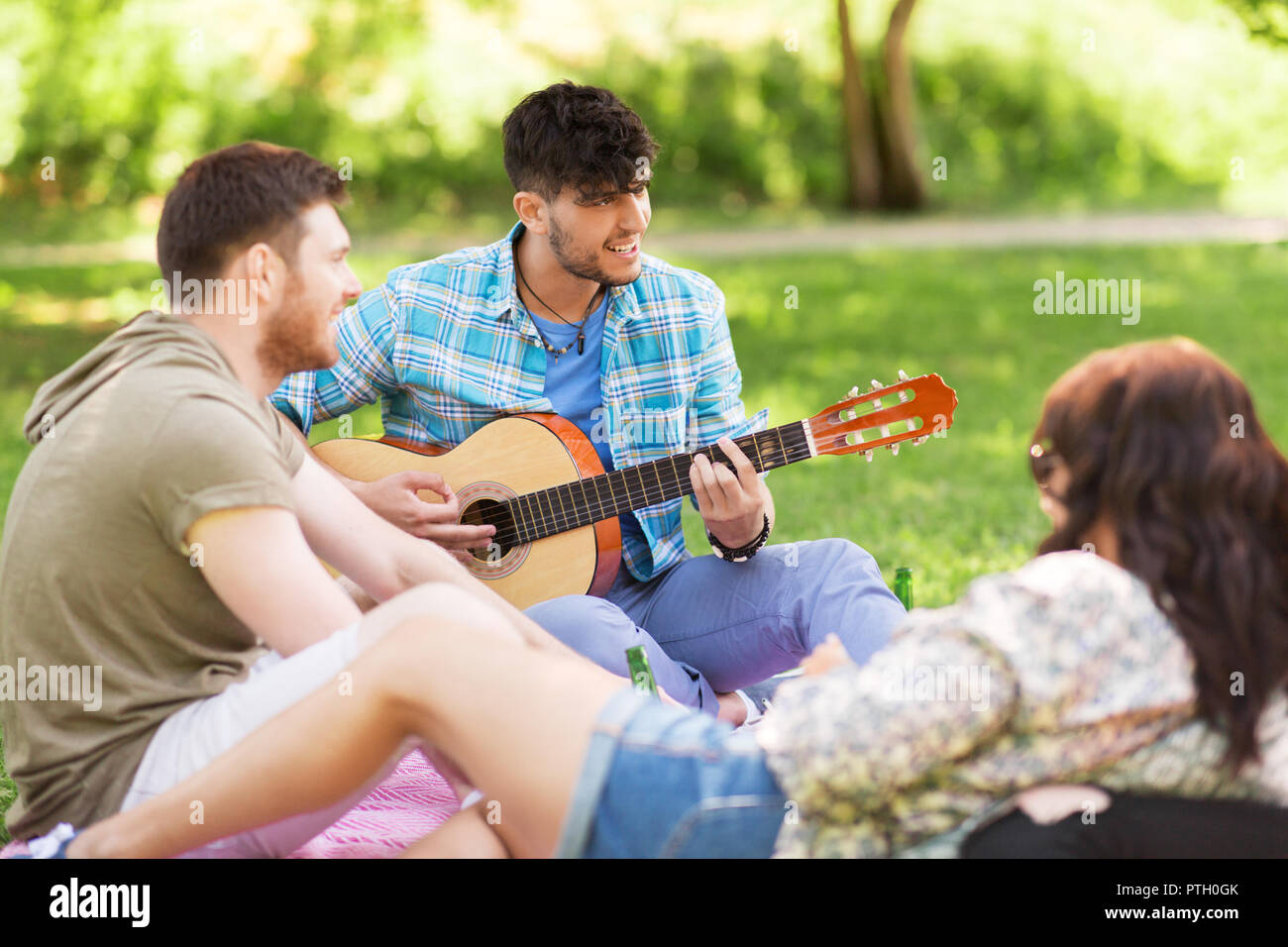 Amici a suonare la chitarra al picnic nel parco di estate Foto Stock