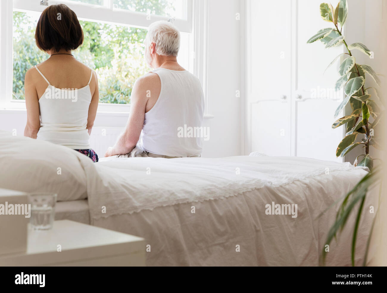 Riflessivo coppia senior seduta sul letto a guardare fuori dalla finestra Foto Stock
