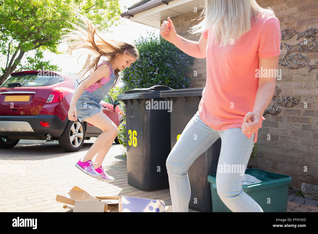 Madre e figlia giocoso rompendo il cartone per il riciclaggio al di fuori casa Foto Stock