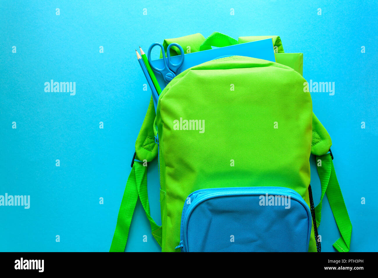Si torna a scuola concetto. Zaino verde con forniture scolastiche su sfondo blu. Vista dall'alto. Spazio di copia Foto Stock