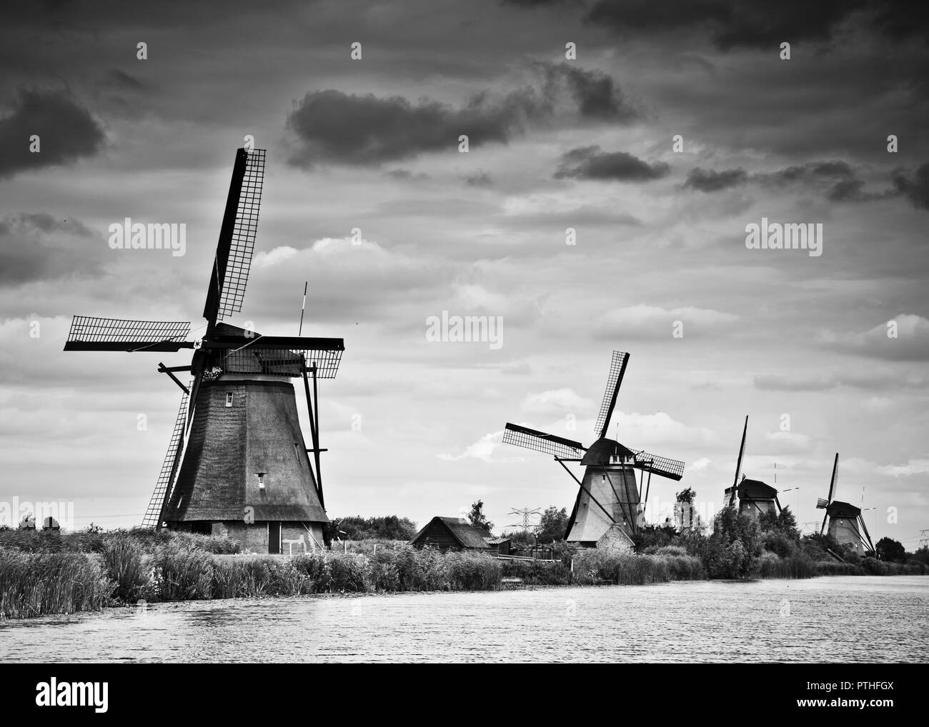 Mulini a vento olandesi tradizionali sulla riva del canale allineati riducendo all'orizzonte, contro un cielo oscuro, graduato nuvoloso, Kinderijk, Olanda, Foto Stock