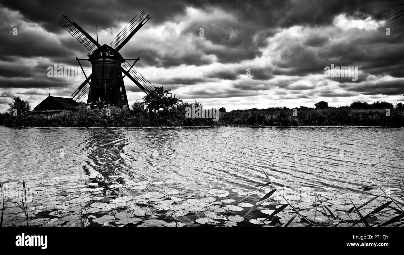 Immagine artistica in bianco e nero del tradizionale mulino a vento olandese con tetto di paglia sulla riva del canale, contro un cielo nuvolato tempesta, Kinderijk, Olanda, Foto Stock