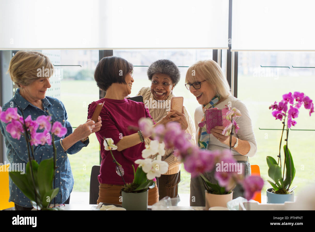 Felici le donne anziane con i telefoni con fotocamera godendo di decorazione floreale di classe Foto Stock
