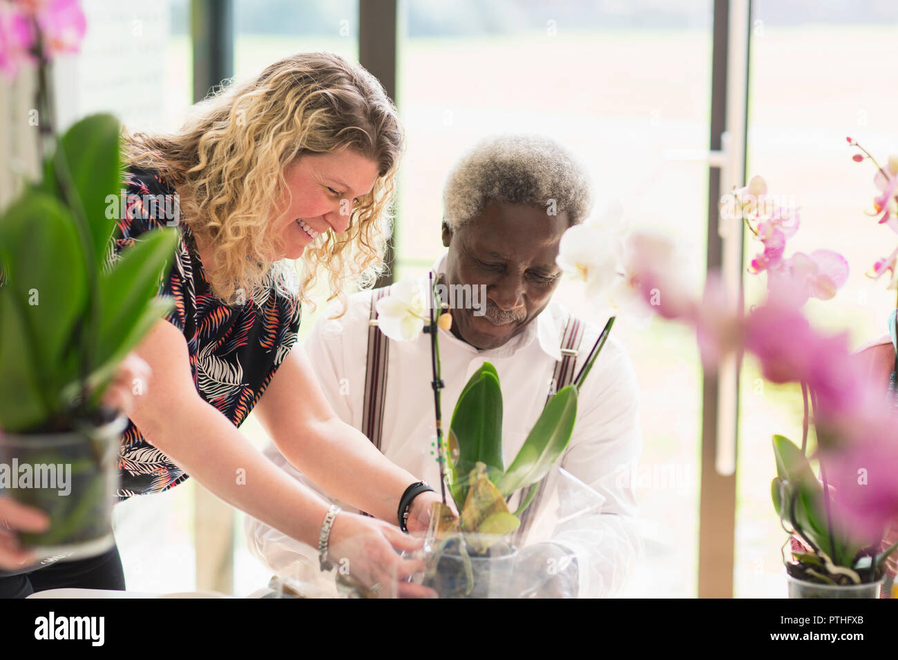 Femmina aiutando istruttore senior attivo uomo nella decorazione floreale di classe Foto Stock