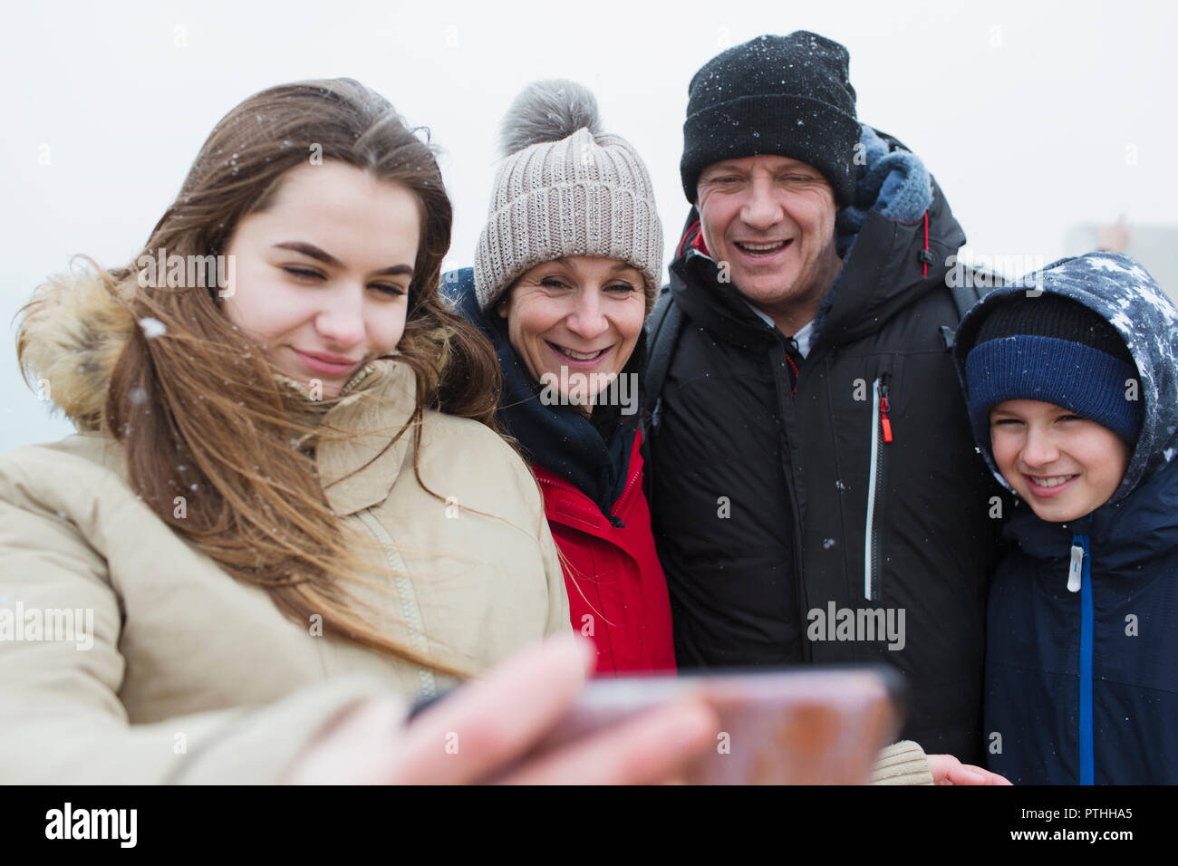 La caduta della neve sulla famiglia sorridente tenendo selfie Foto Stock