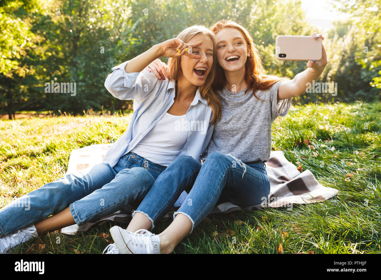 Immagine di due belle ragazze studenti indossano jeans seduto su erba in  estate park e tenendo selfie sul telefono cellulare Foto stock - Alamy