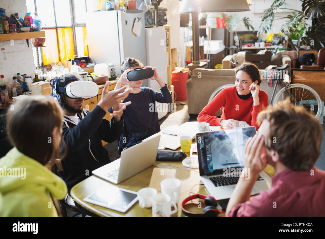 Giovane studente del collegio amici che studiano, utilizzando la realtà virtuale simulator bicchieri al tavolo da cucina in appartamento Foto Stock