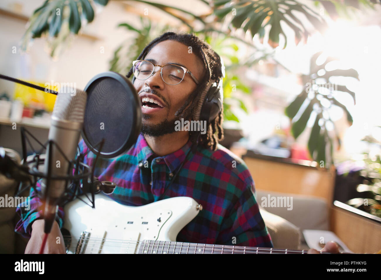 Giovane uomo la registrazione della musica, suonare la chitarra e cantare nel microfono Foto Stock